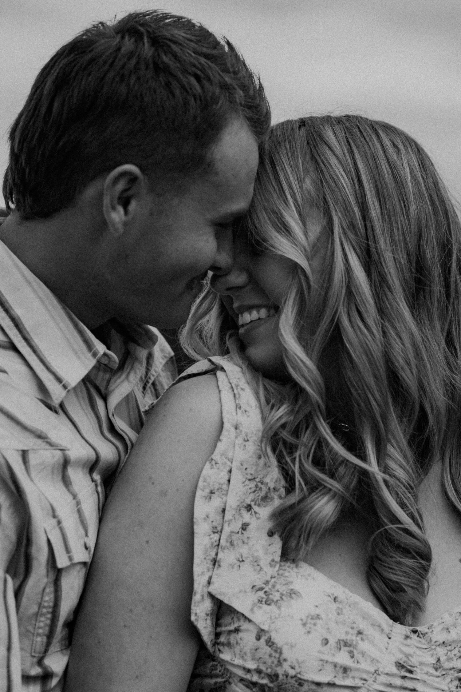 Intimate black and white portrait of a couple sharing a tender moment with their foreheads touching and genuine smiles.