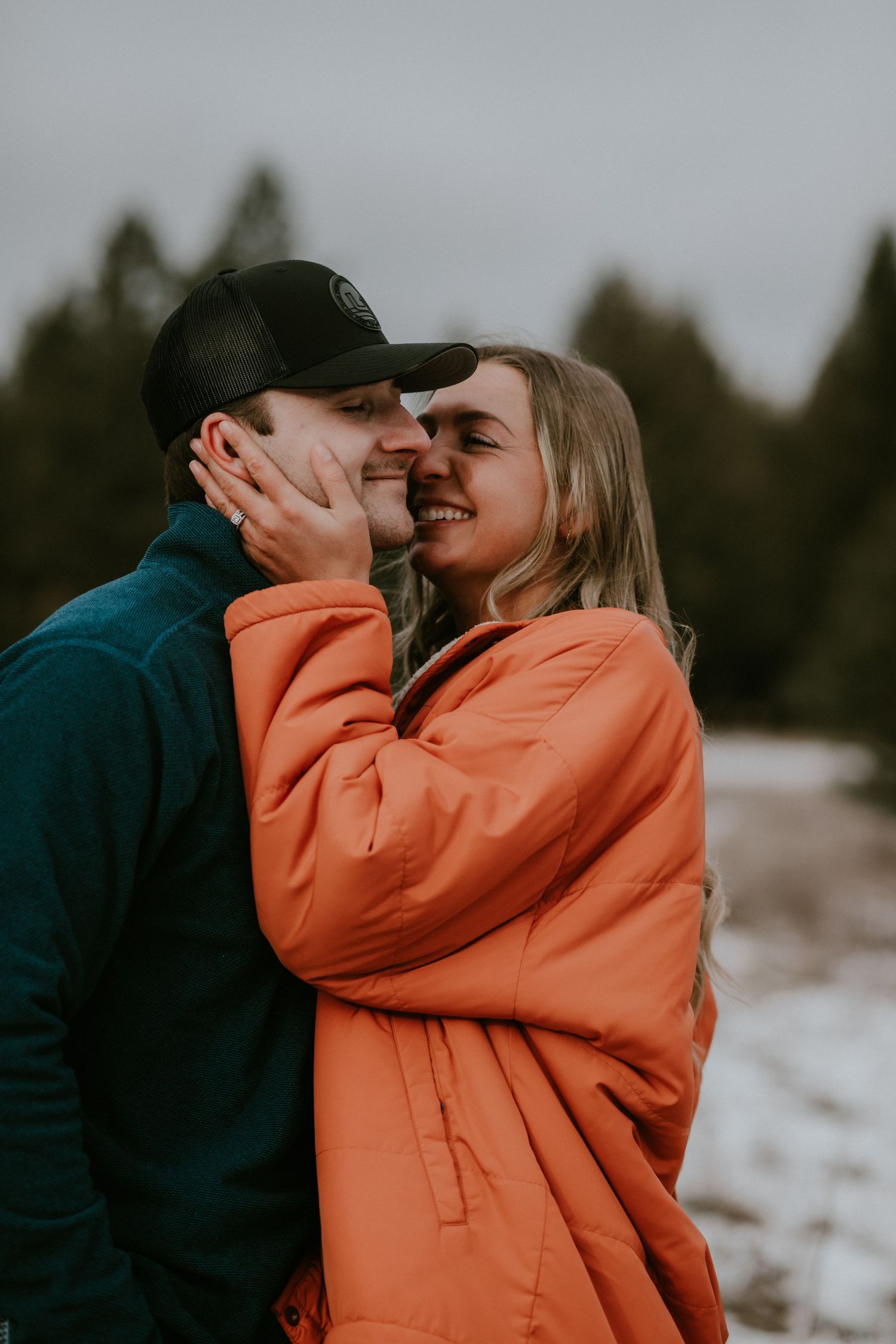 A couple shares an intimate moment outdoors in winter, with one wearing a bright orange coat and the other in dark clothing.