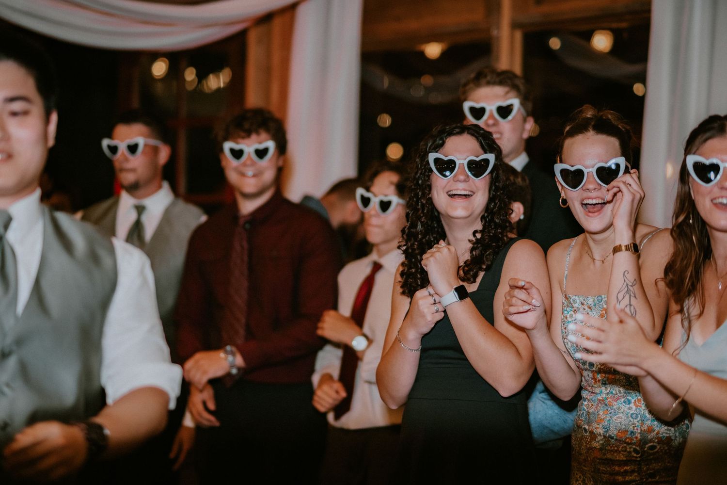 People wearing sunglasses dancing and celebrating at a lively party gathering.