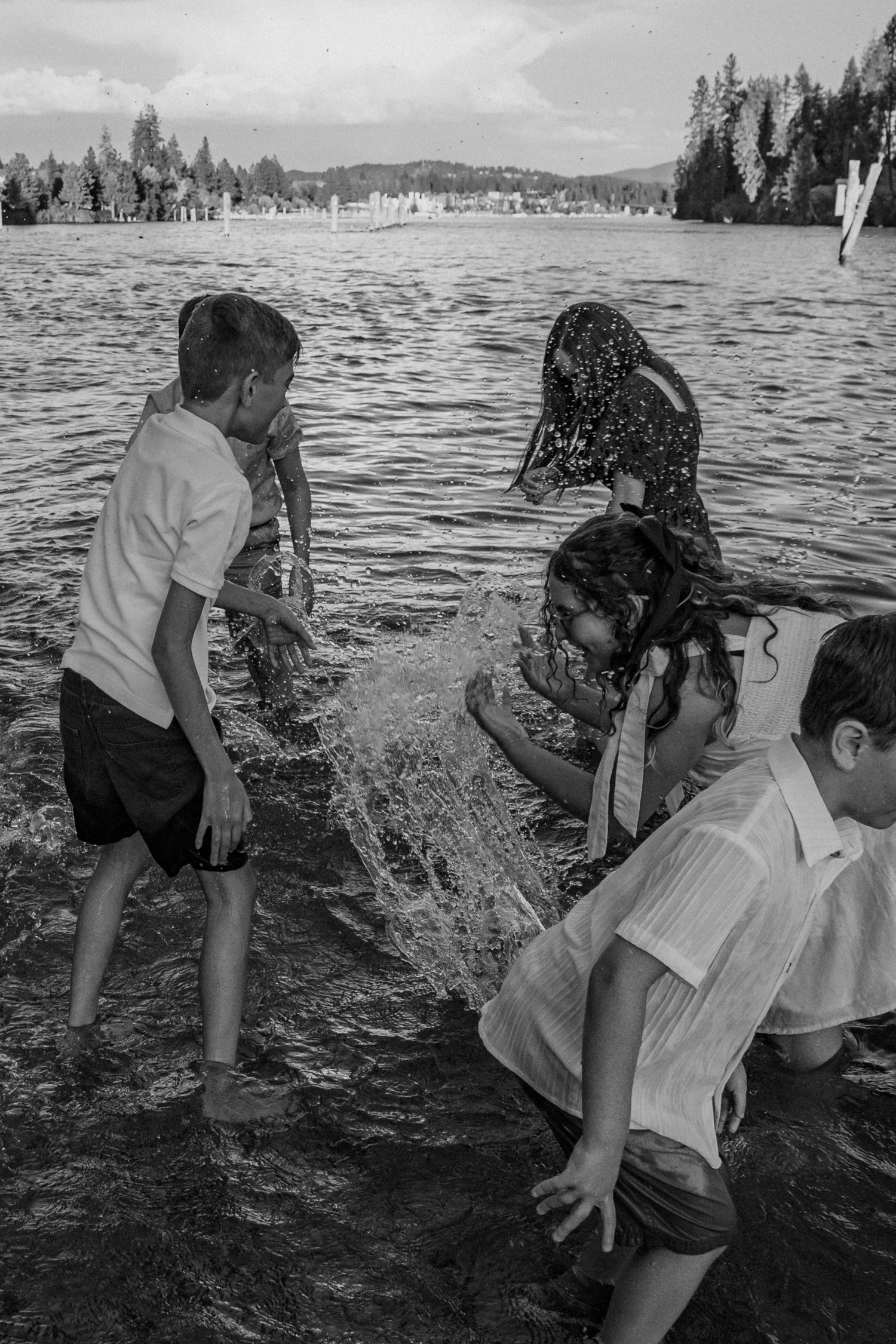 A sequence of black and white photos showing people playing and splashing in the water at a lake with trees in background.
