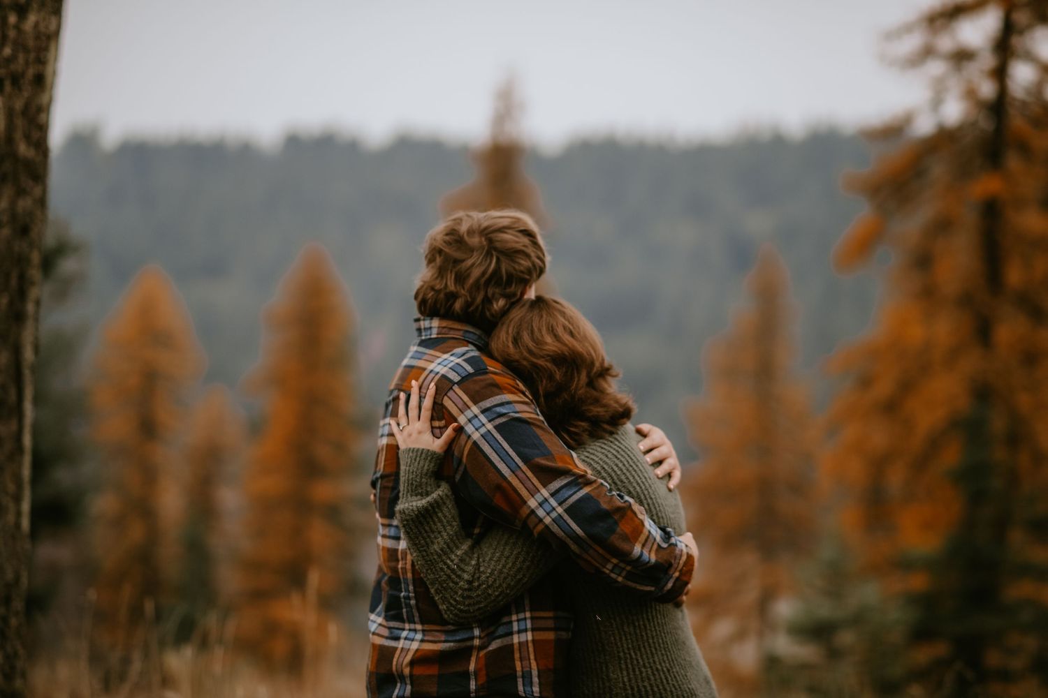People embracing in a forest with orange autumn larch trees and misty mountains in the background.