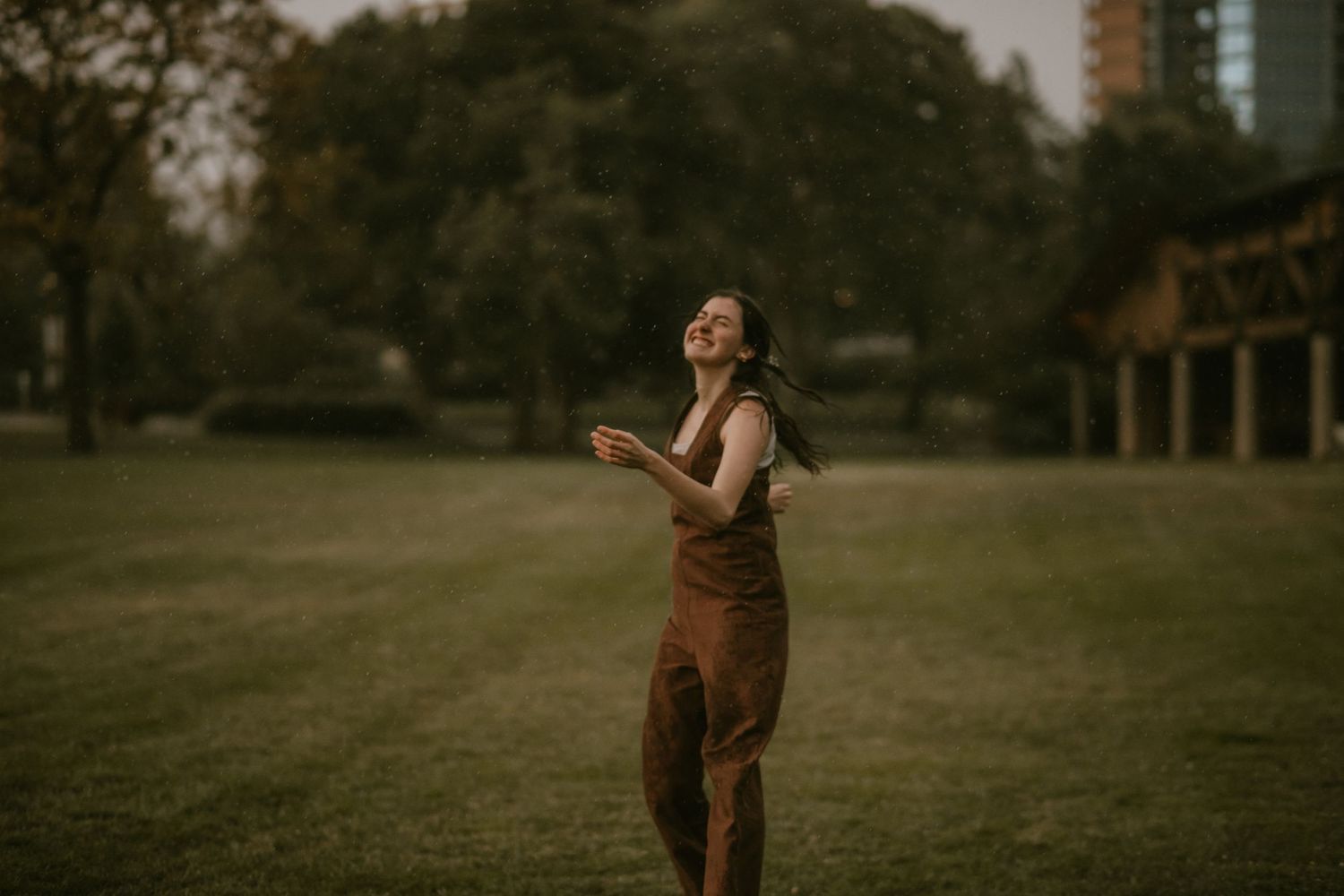 A couple in vintage brown outfits hold hands while walking together in a grassy outdoor setting during golden hour.