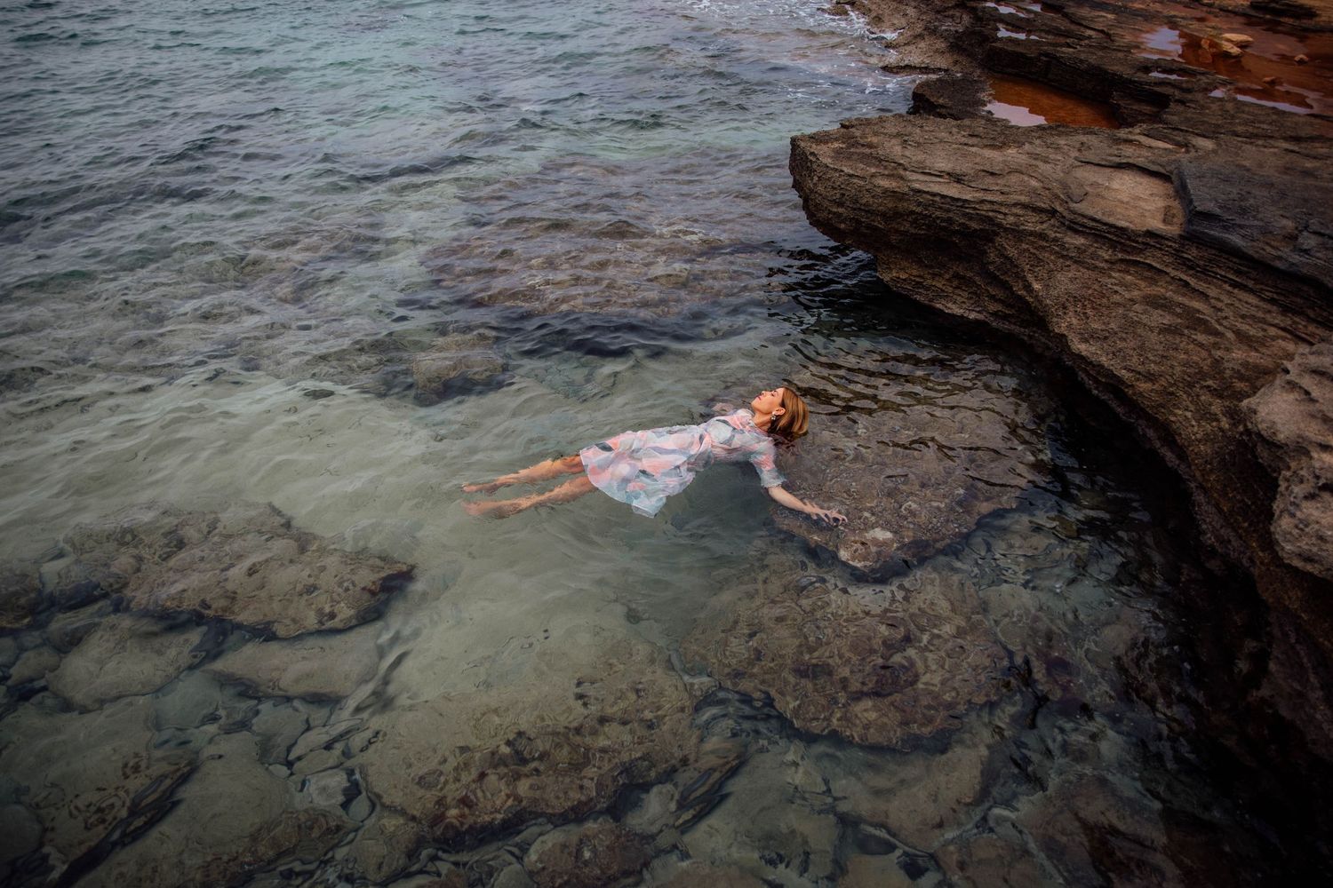 Women floating peacefully in clear turquoise water by rocky coastal cliffs. Spiritual photography Mallorca: Capturing serenity and connect