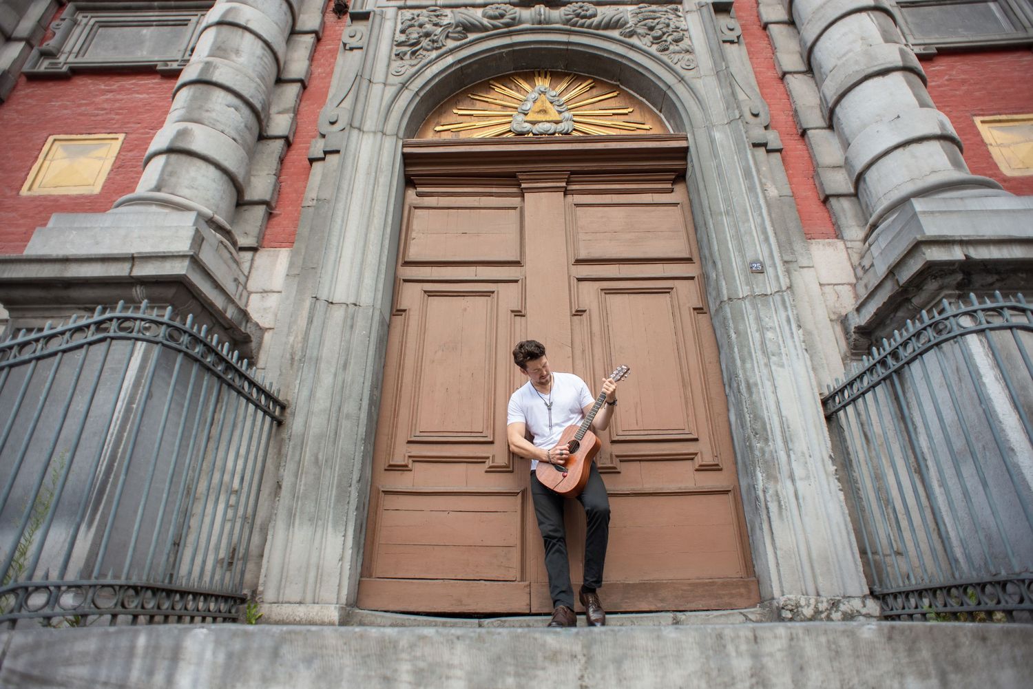 À Liège, dans le quartier Hors-Château, portrait d’un homme jouant de la guitare devant un bâtiment à l’architecture impressionnante