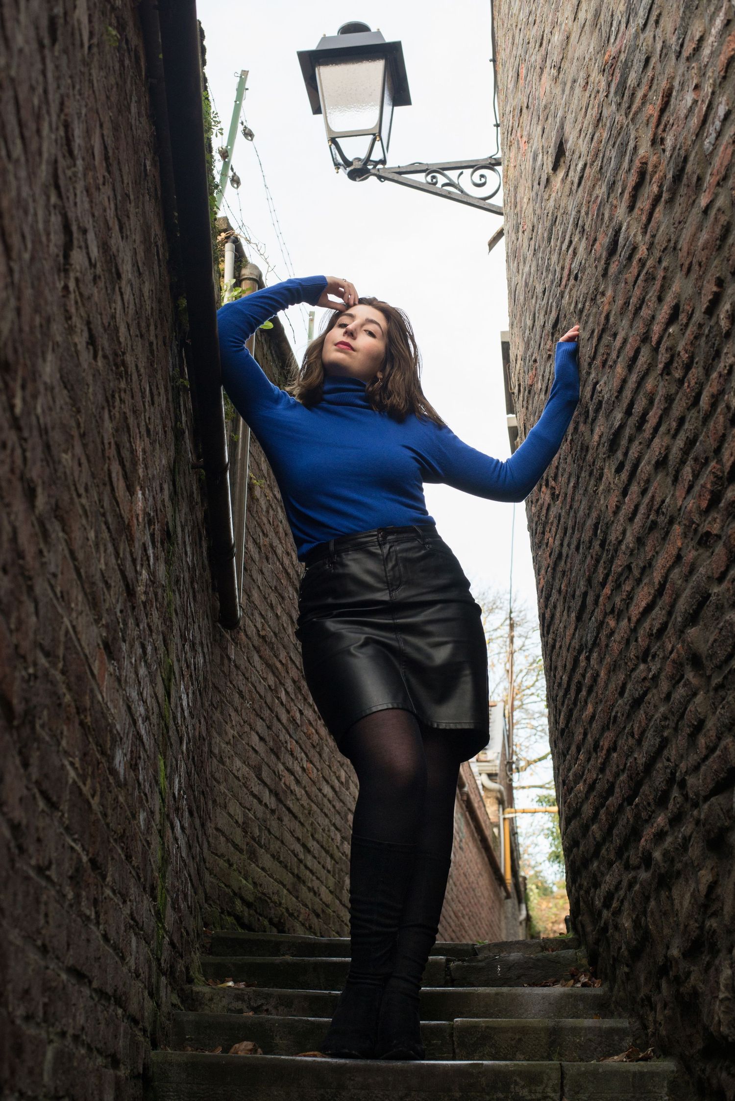 À Liège, dans les impasses des coteaux de la Citadelle, portrait d’une femme debout près d’un lampadaire lors d’une séance photo urbaine
