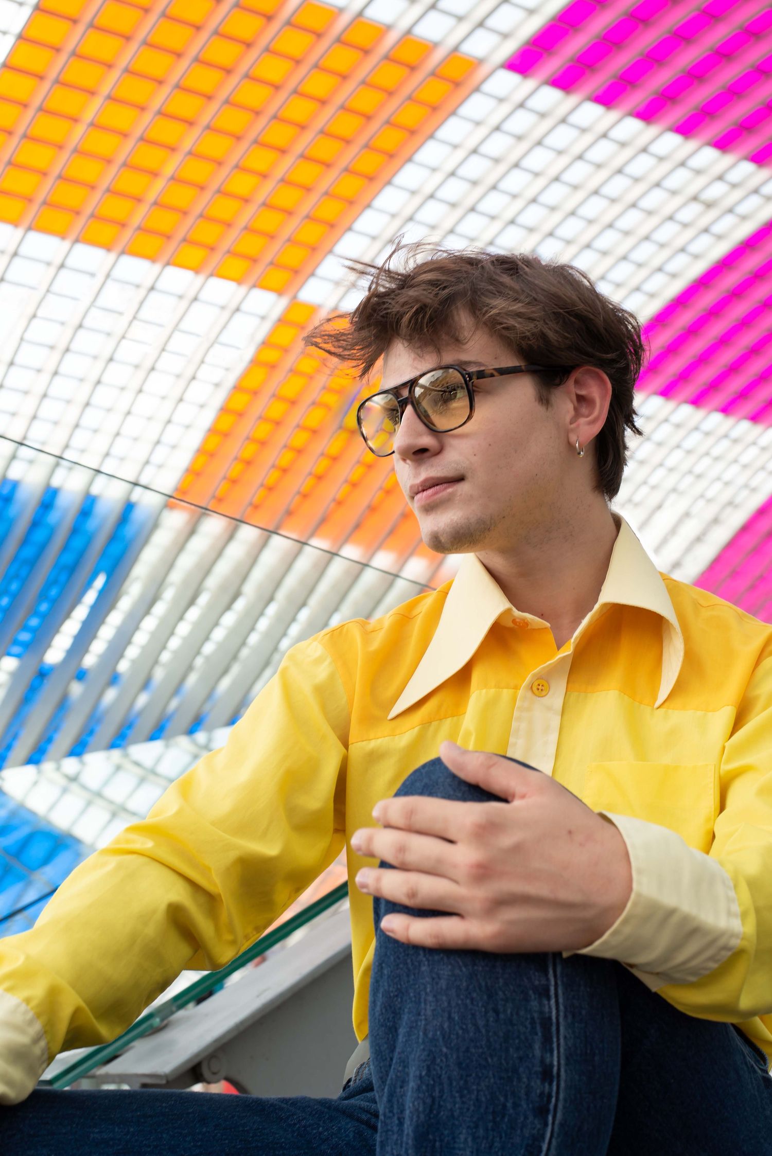 À Liège, à la gare des Guillemins, portrait d’un homme assis dans les escaliers avec l’œuvre colorée de Daniel Buren en arrière-plan