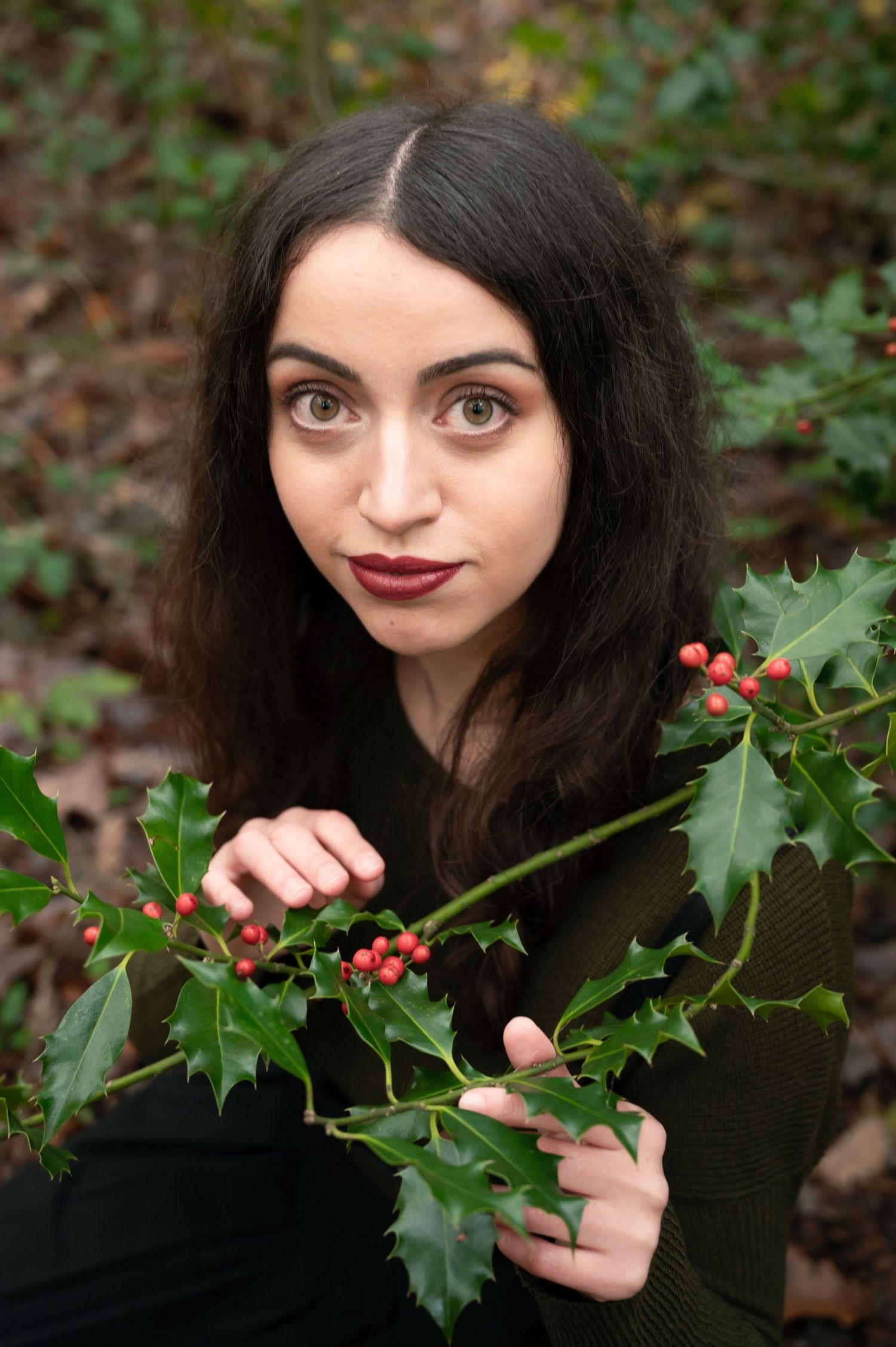 À Liège, au bois du Sart-Tilman, portrait d’une femme tenant une branche de houx et souriant face à la caméra lors d’une séance photo