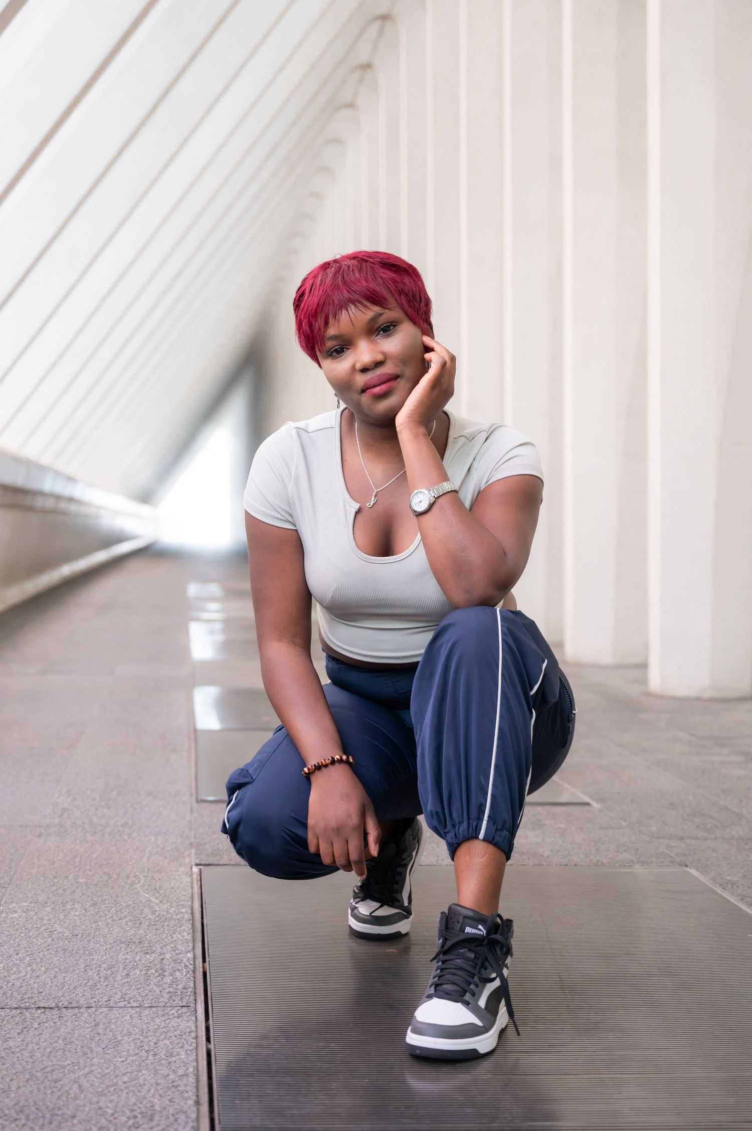 À Liège, à la gare des Guillemins, portrait d’une femme accroupie, main sur le menton, regardant la caméra dans une allée à l’architecture m