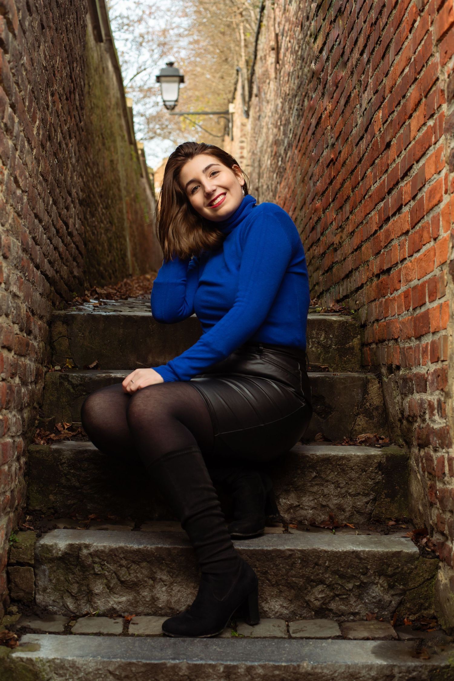 À Liège, dans les impasses des coteaux de la Citadelle, portrait d’une femme assise dans les escaliers, souriante, lors d’une séance photo e
