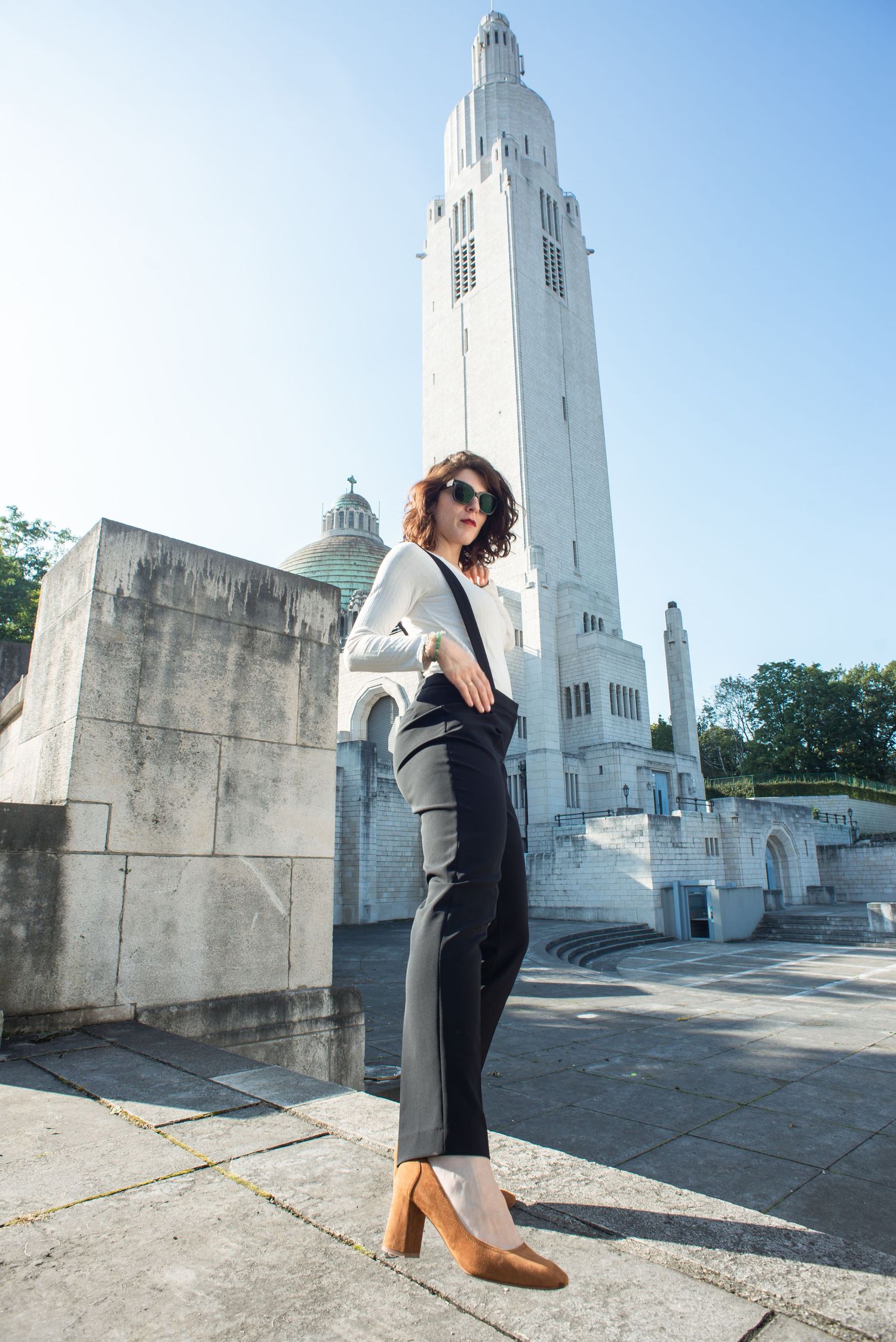 À Liège, au mémorial interallié de Cointe, portrait d’une femme photographiée debout avec la jambe tendue devant l’architecture du monument
