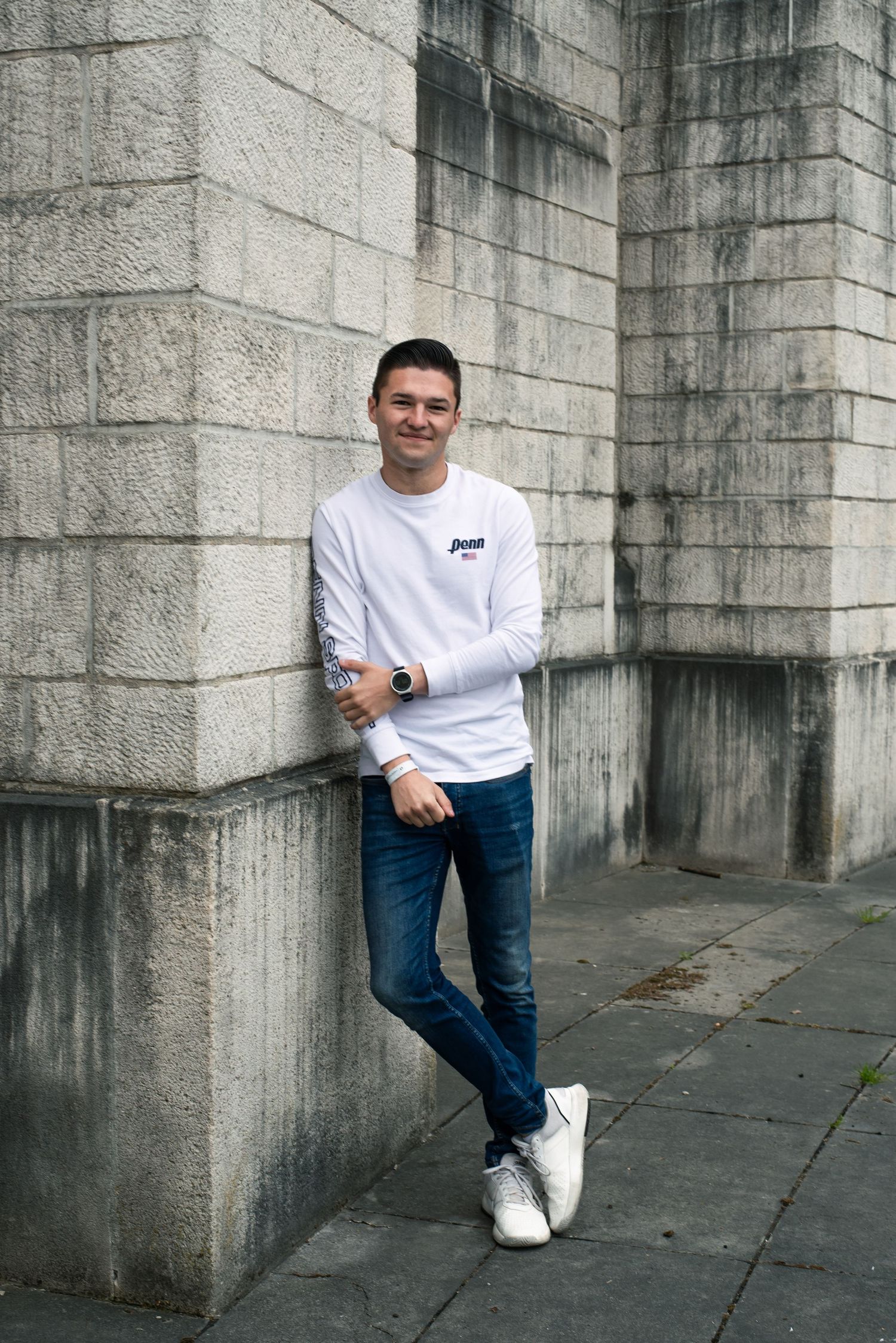 À Liège, au mémorial interallié de Cointe, portrait d’un homme posé contre le mur du monument, regardant la caméra avec un sourire naturel