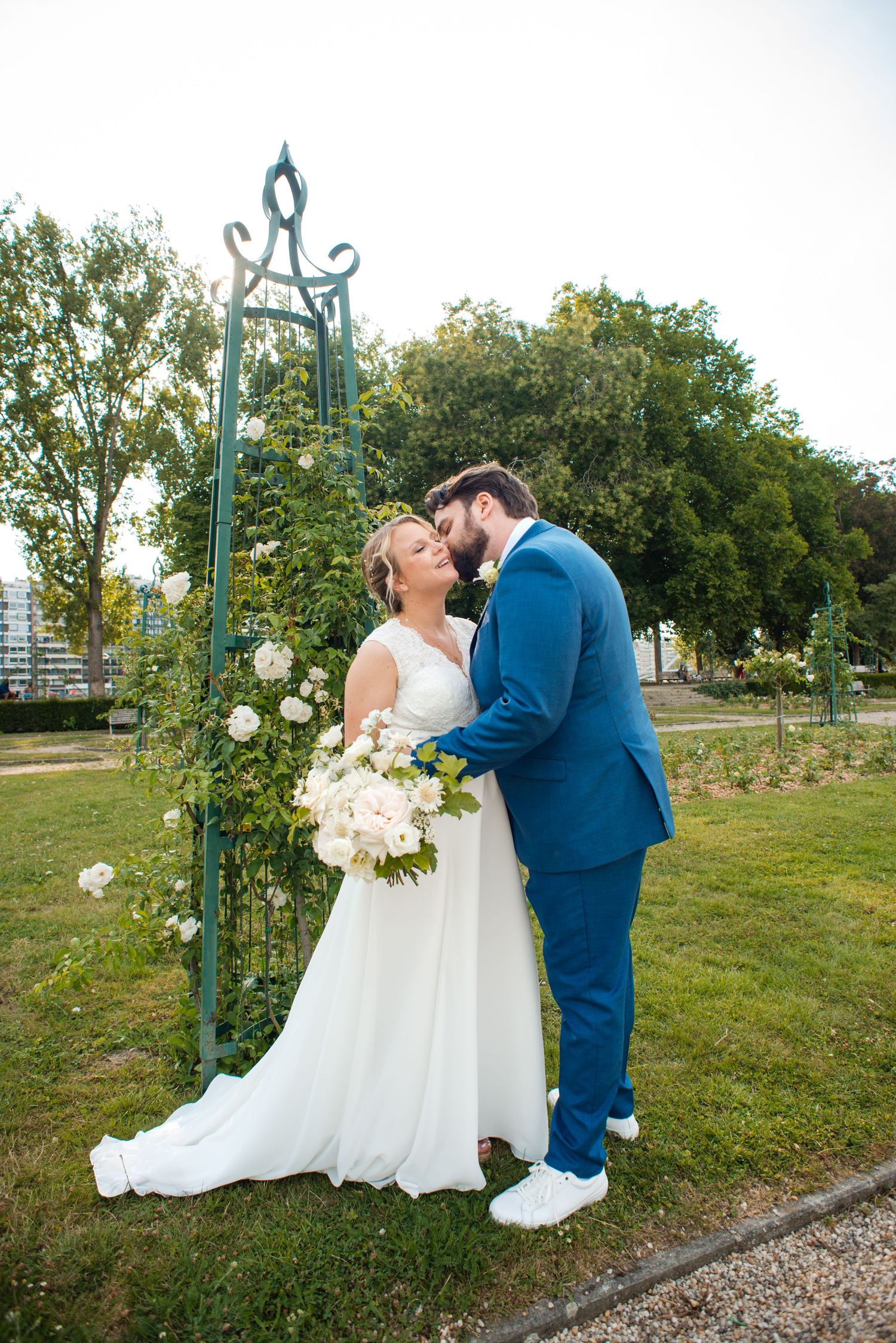 Séance photo de couple de mariés s’embrassant dans le parc de la Boverie à Liège avec des roses blanches
