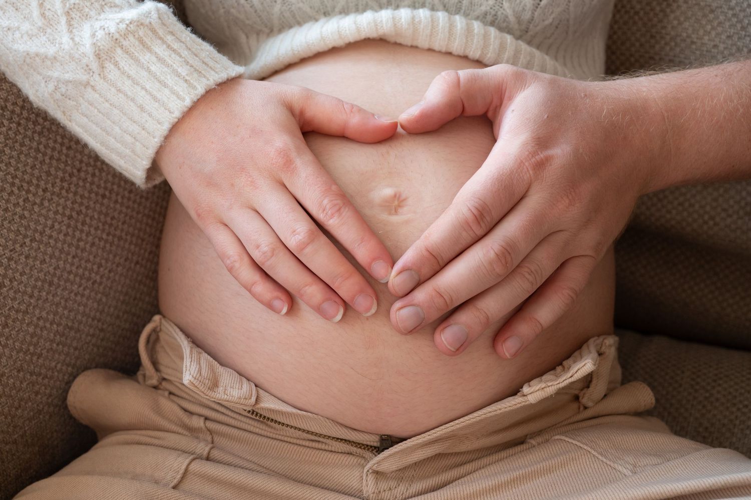À Saint-Hubert, détail du ventre de la future maman avec les mains en forme de cœur lors d’une séance photo grossesse