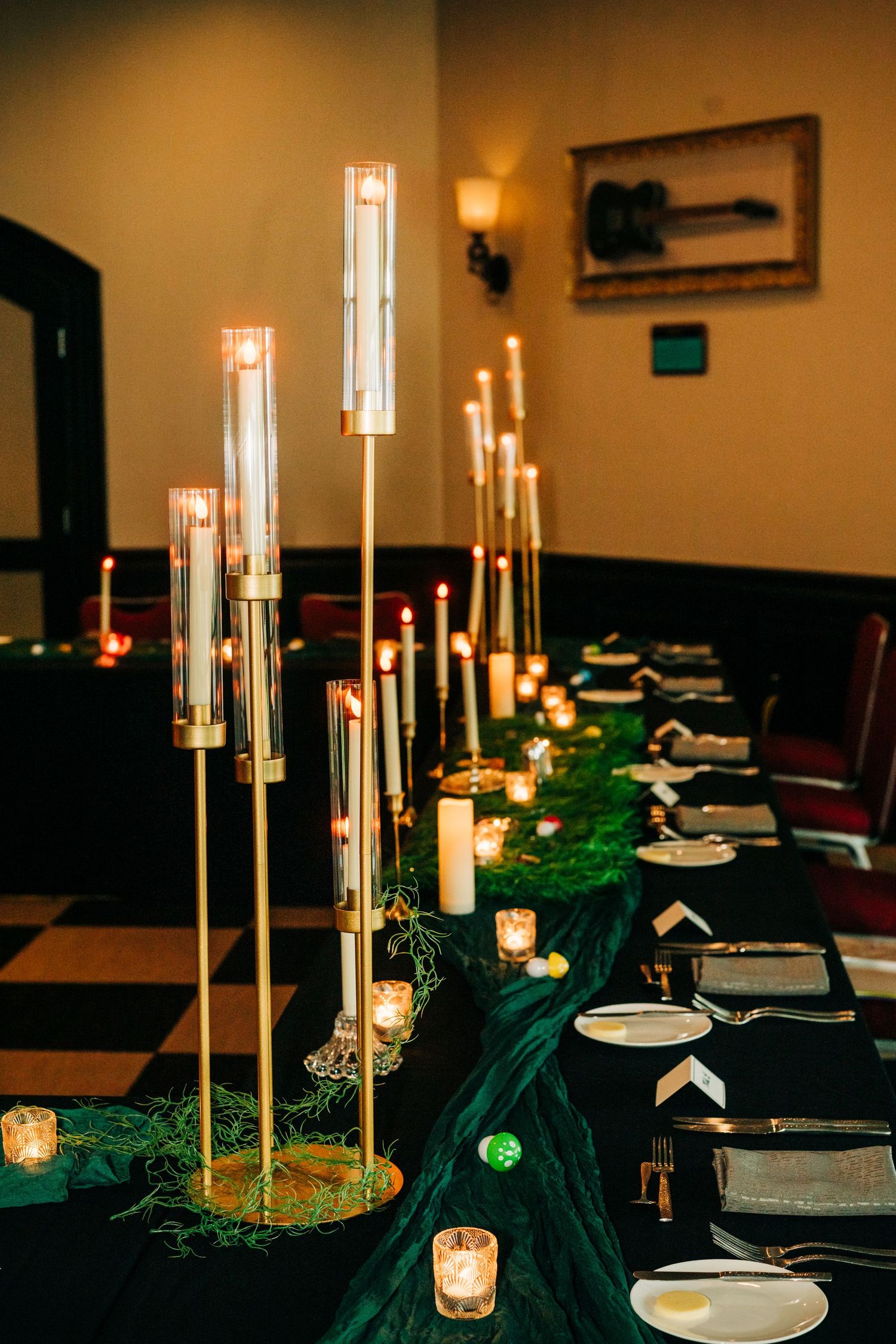 Elegant wedding reception table with gold candelabras, green velvet runner, white candles, and black-and-white checkered floor.