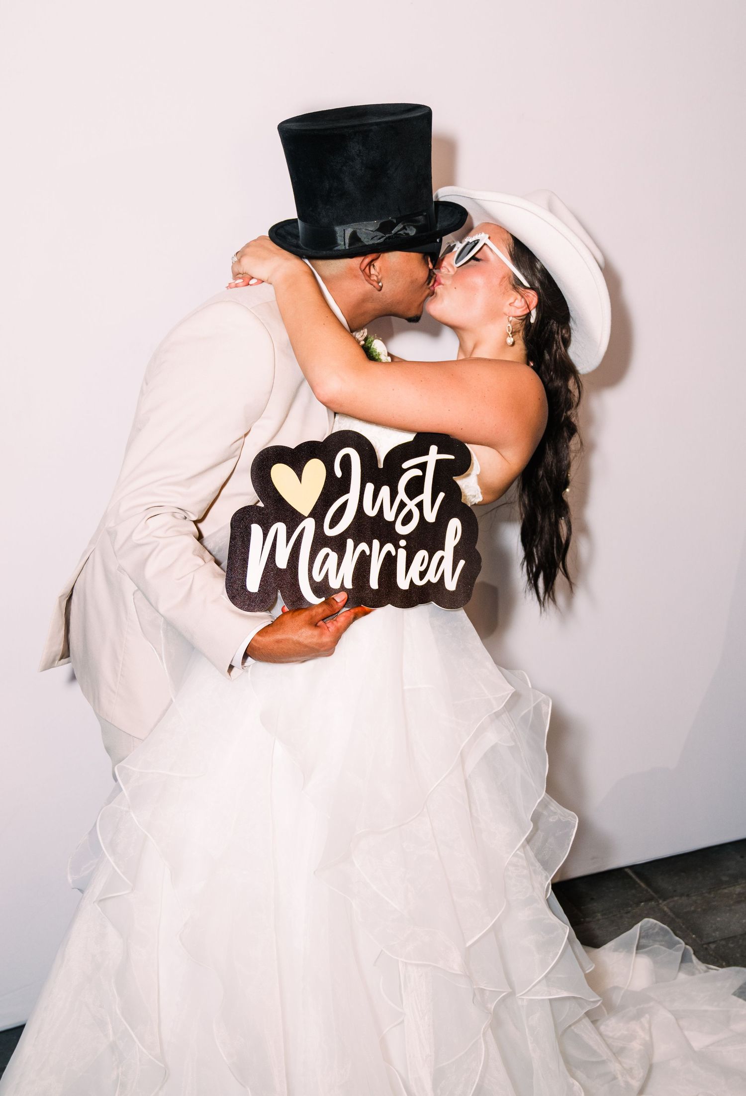 Newlywed couple kissing while holding a Just Married sign, bride in white gown and groom in top hat.