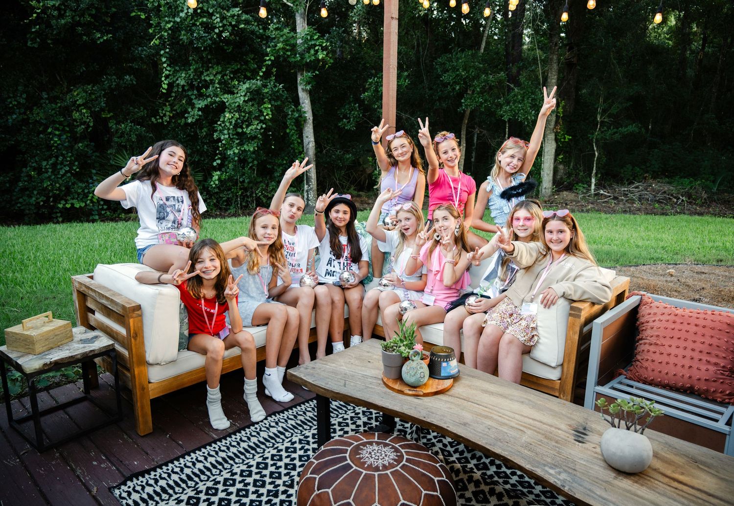 Group of teenage girls posing together on outdoor patio furniture at a backyard party with string lights.