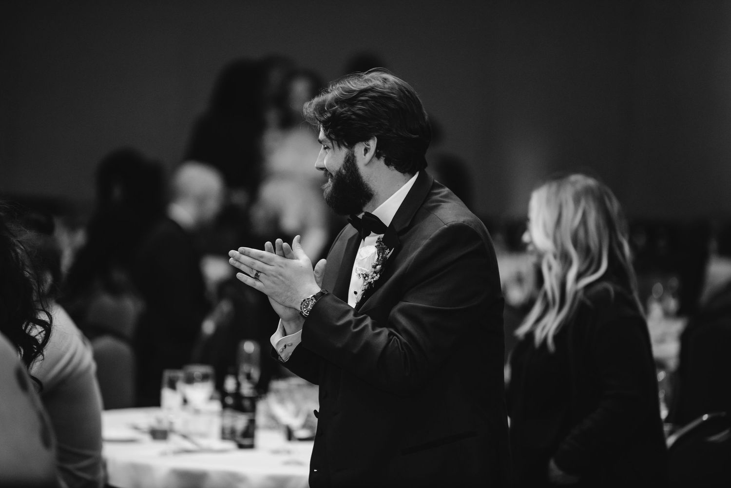 Man in tuxedo clapping at elegant wedding reception in black and white photography.