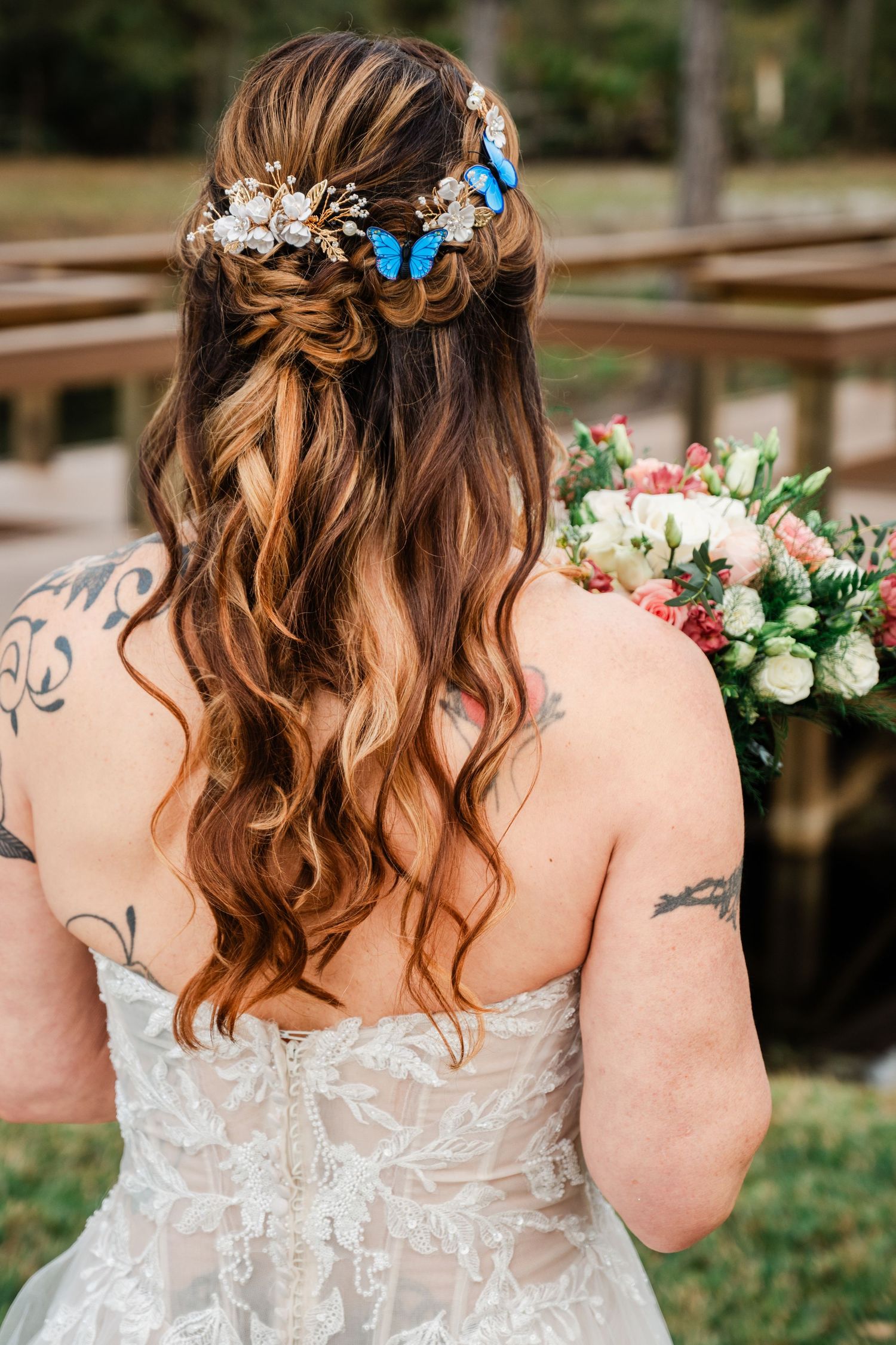Bride with half-up hairstyle adorned with blue butterflies, holding bouquet, showing tattoos and lace wedding dress.