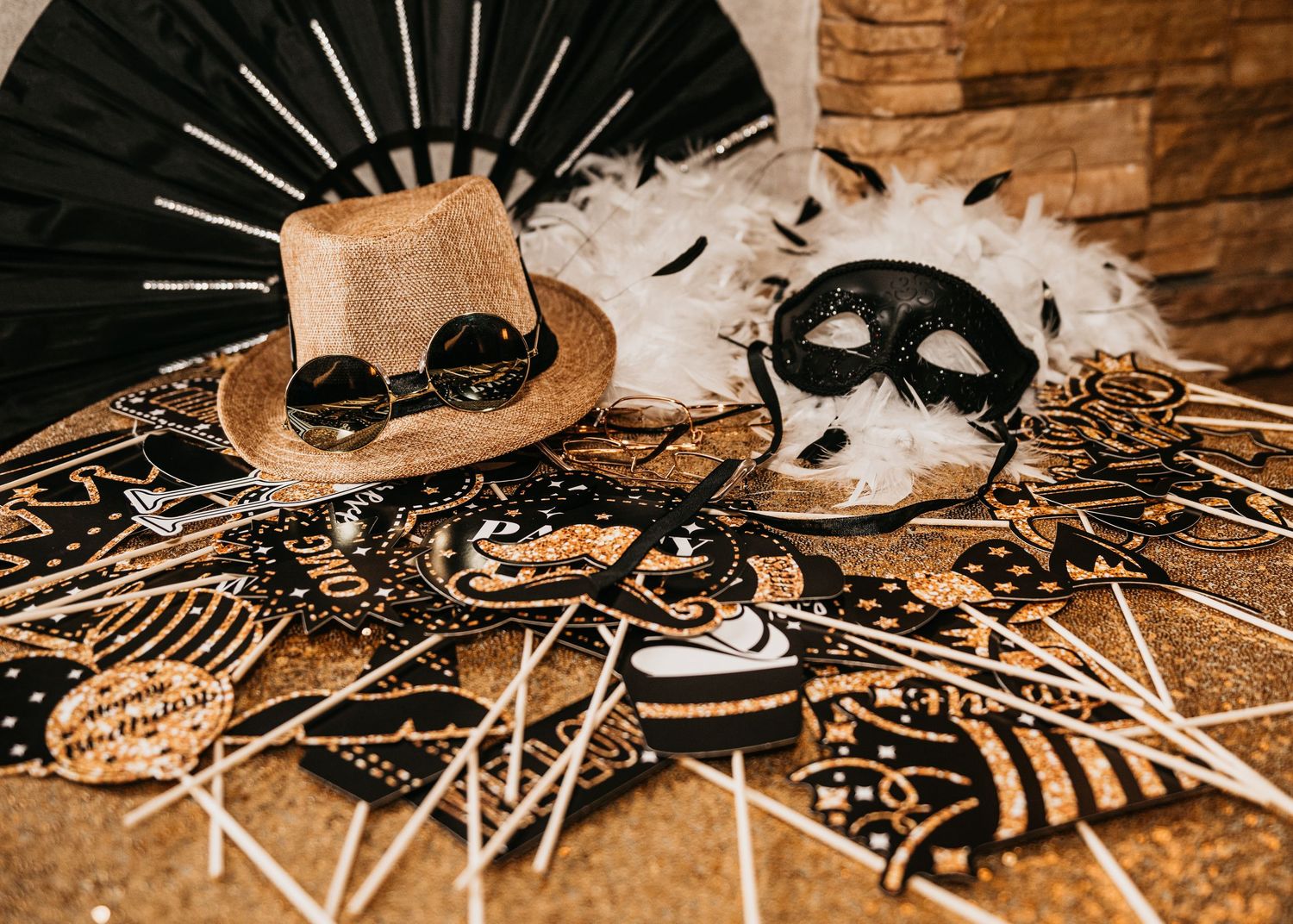 Gold top hat, goggles, black masquerade mask, and festive photo booth props on a decorative black and gold table.
