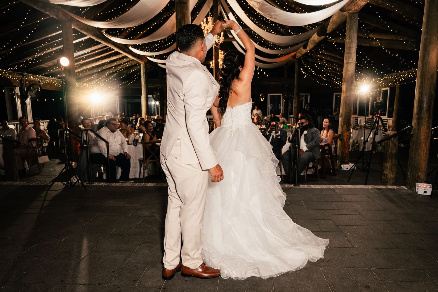 Bride and groom share their first dance under twinkling fairy lights at a romantic wedding reception.