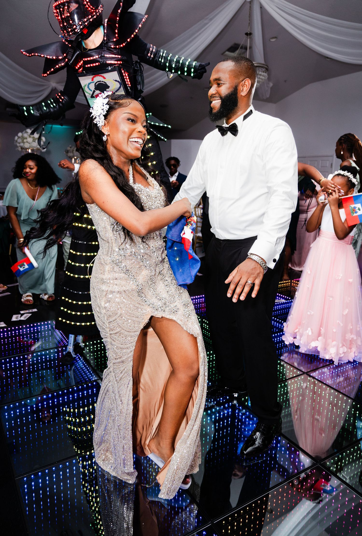 Couple dancing elegantly on LED dance floor at formal event, woman in silver gown, man in white tuxedo shirt.