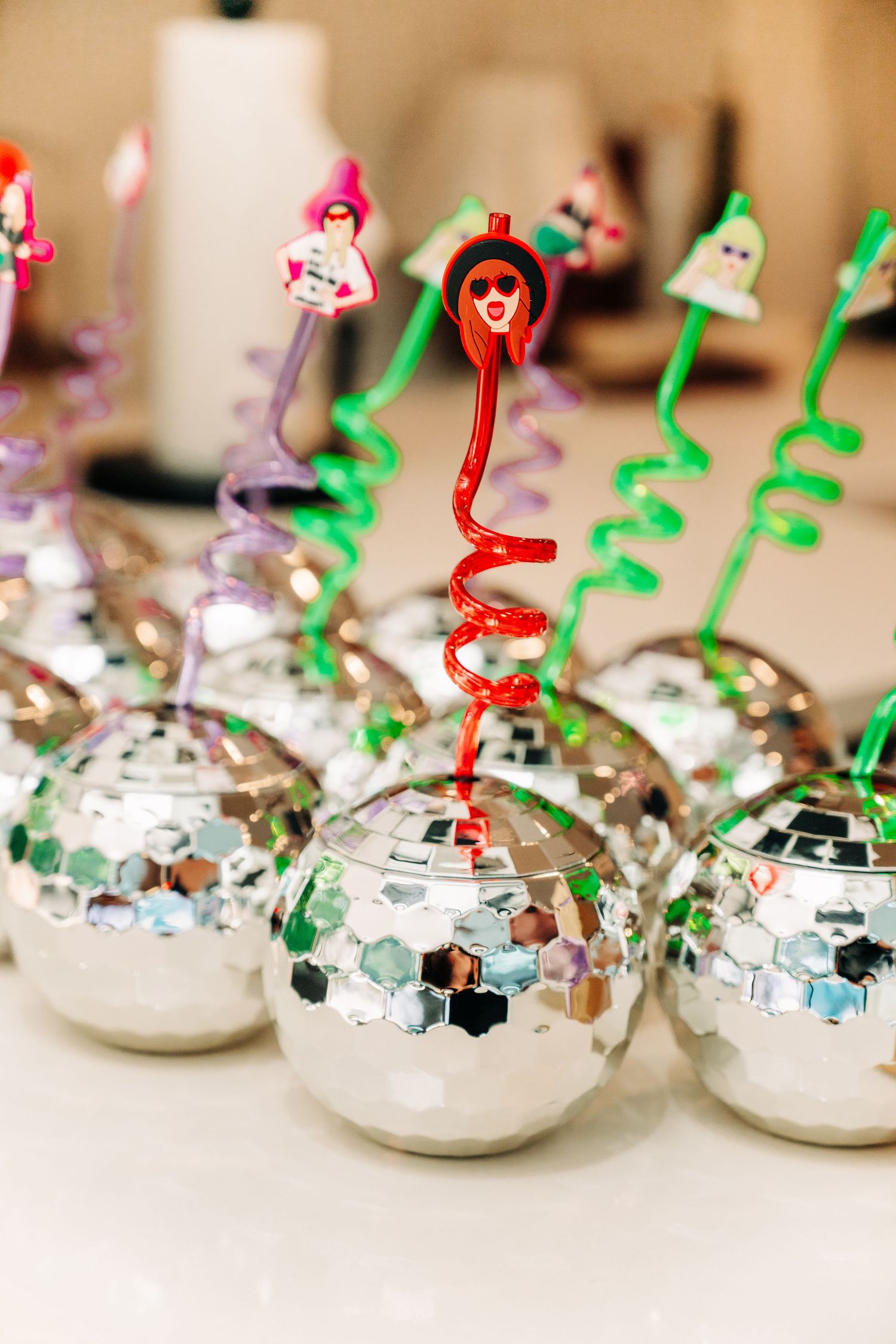 Disco ball cups with colorful spiral straws and fun character toppers displayed on a white surface for a party.