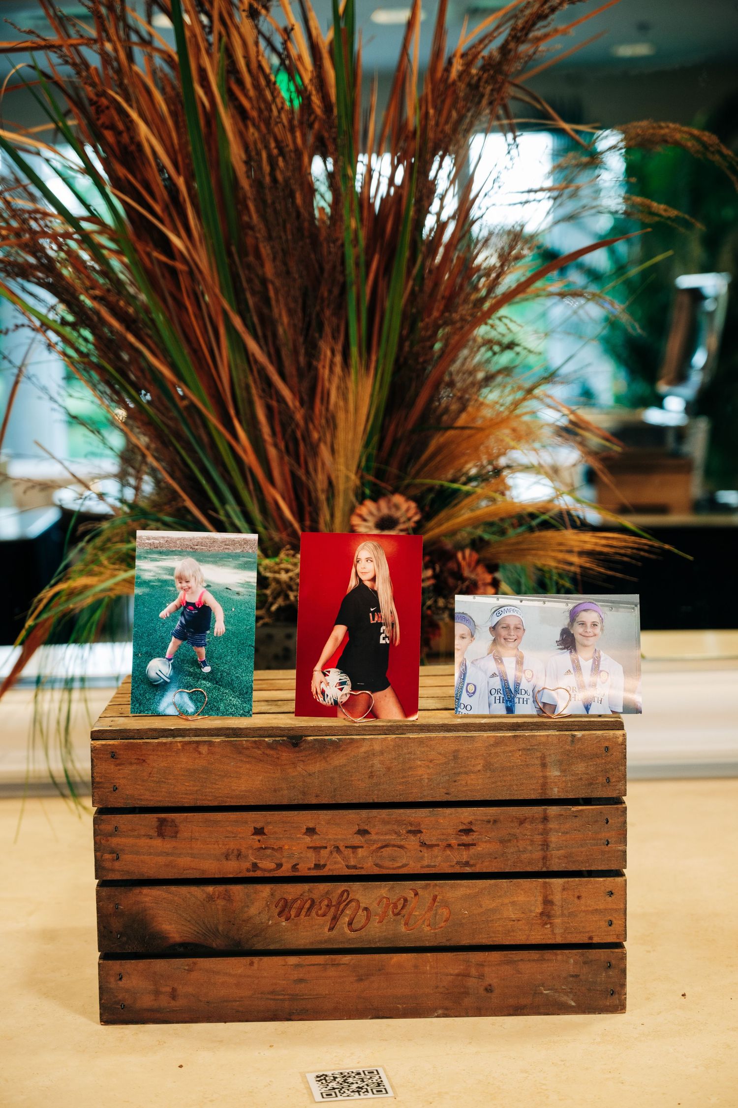 Wooden crate display with three soccer player photos and tall ornamental grass centerpiece at a sports celebration event.