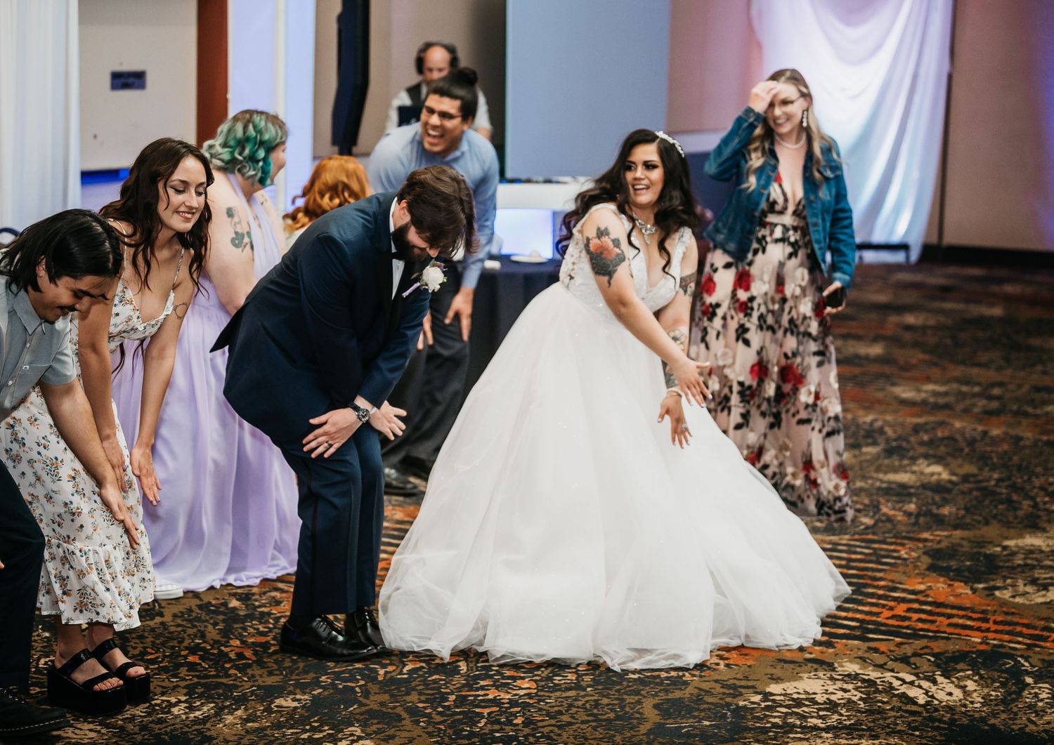 Bride in white ballgown laughing with wedding guests on dance floor at elegant indoor reception.