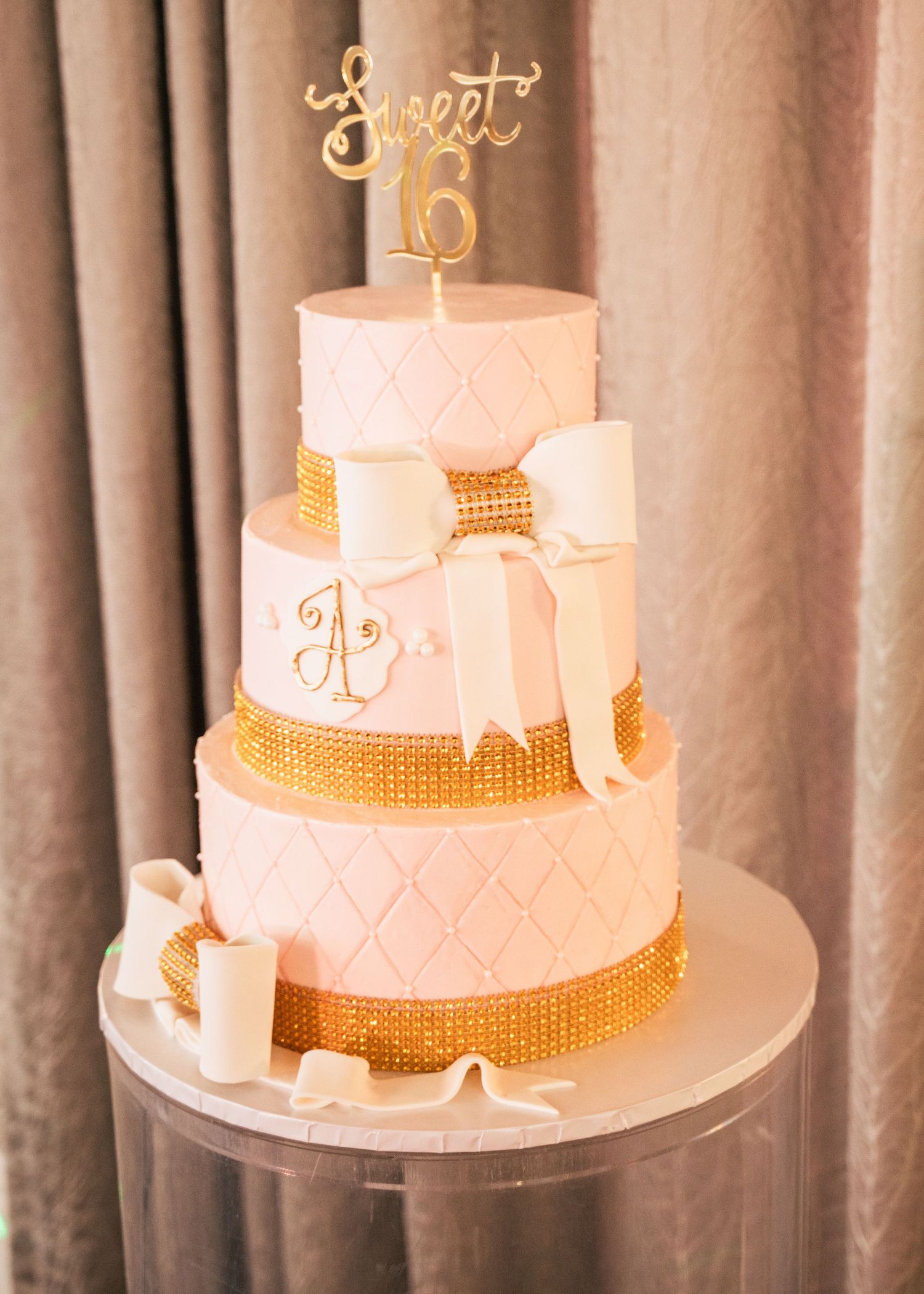 Pink and gold three-tier Sweet 16 birthday cake with bow, quilted fondant, rhinestone bands, and gold cake topper.