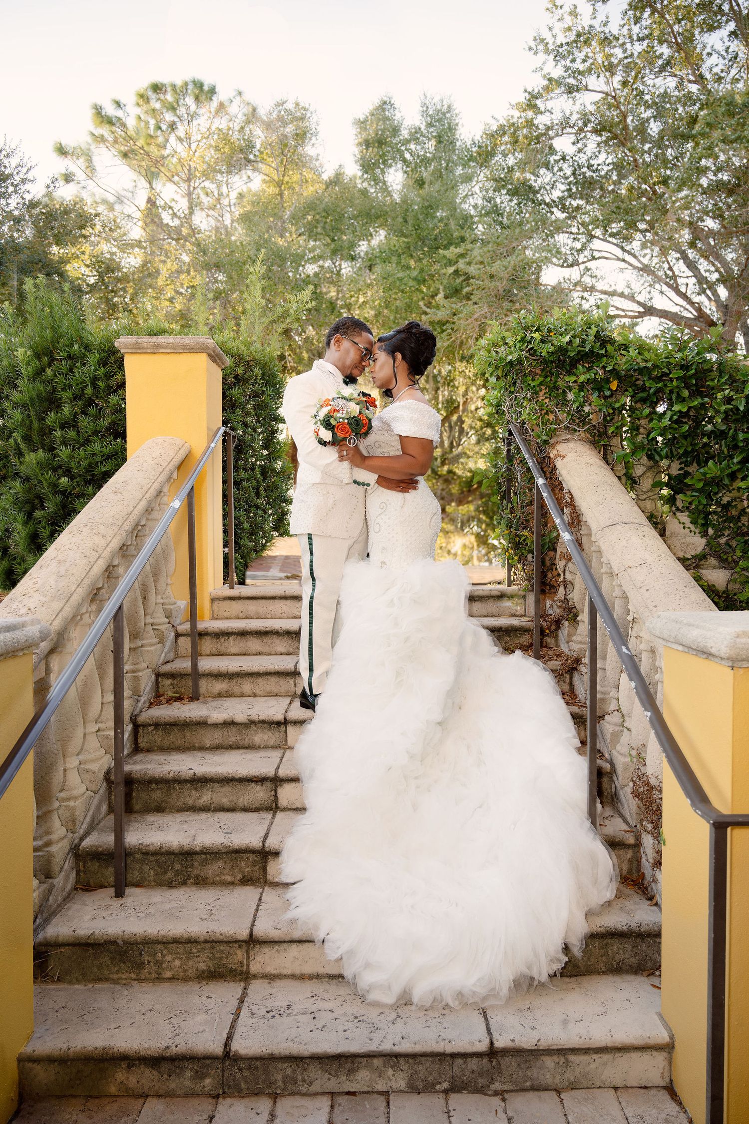 Bride and groom share a romantic moment on stone steps surrounded by lush greenery on their wedding day.