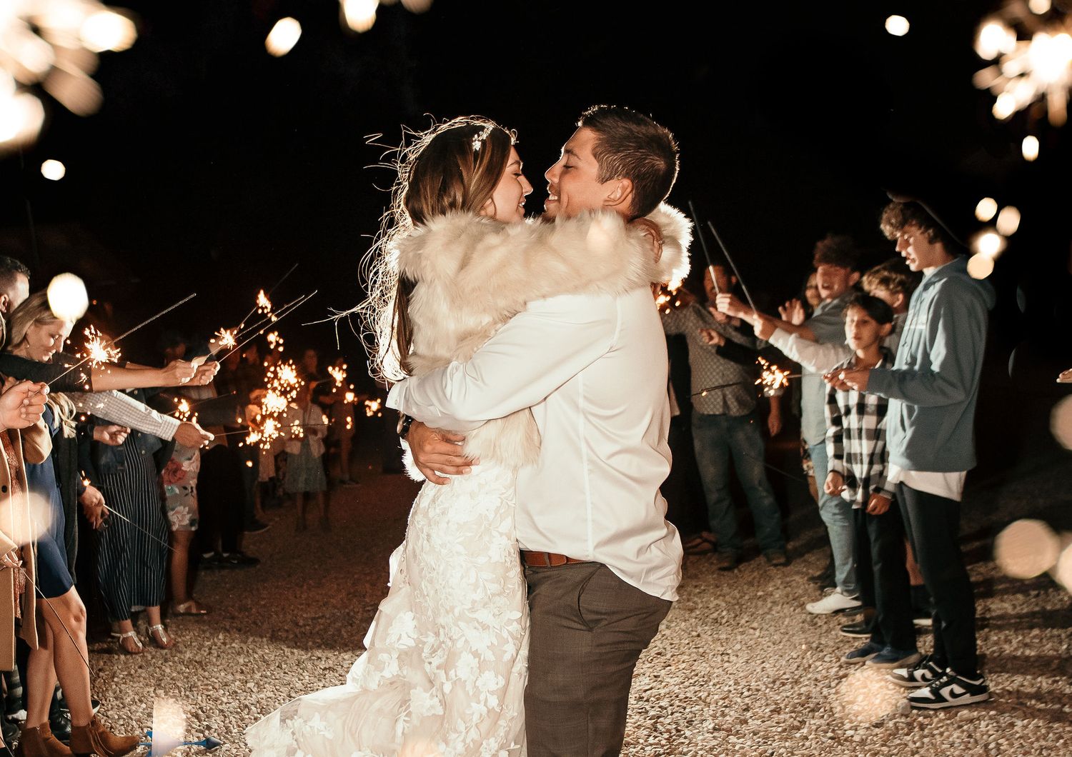 Bride and groom share a romantic kiss during a sparkler send-off at their outdoor evening wedding celebration.