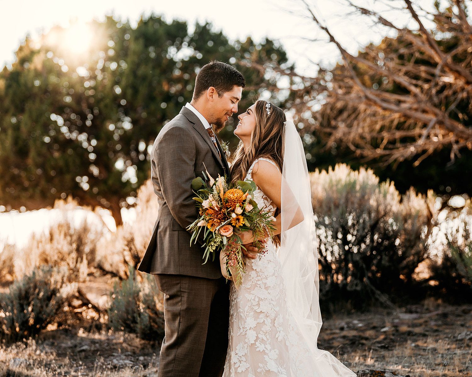 Bride and groom share a romantic kiss outdoors at golden hour, surrounded by desert shrubs and warm autumn wedding bouquet.