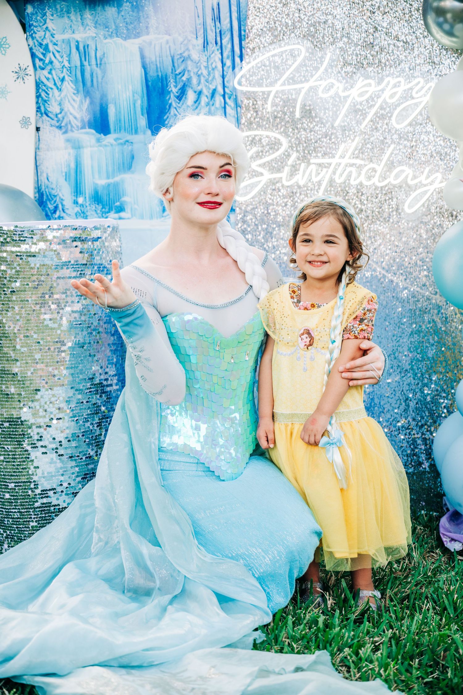 Girl in yellow dress poses with Elsa princess character at a Frozen-themed Happy Birthday party celebration.