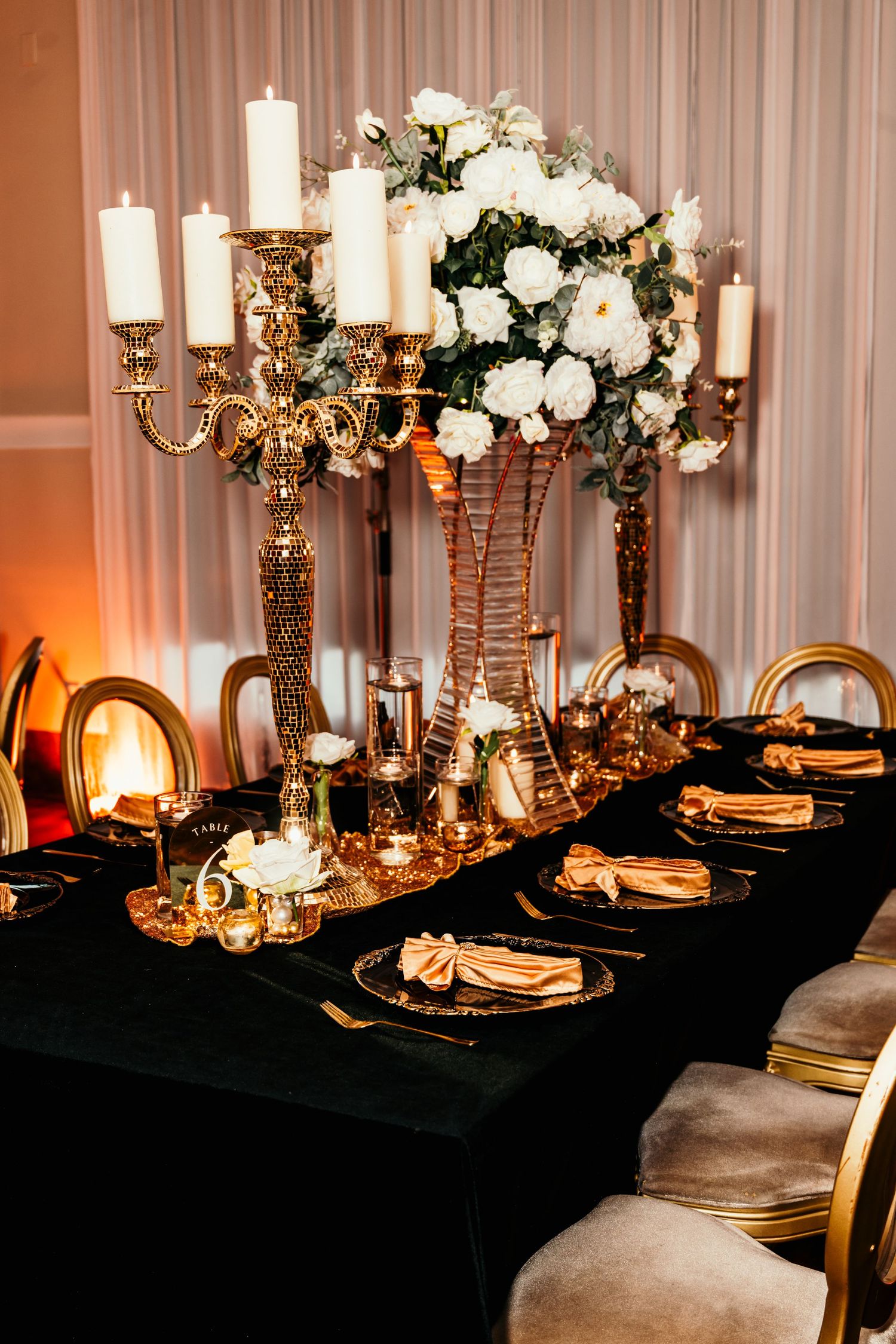 Elegant black and gold wedding reception table with candelabras, white floral centerpiece, and velvet tablecloth.