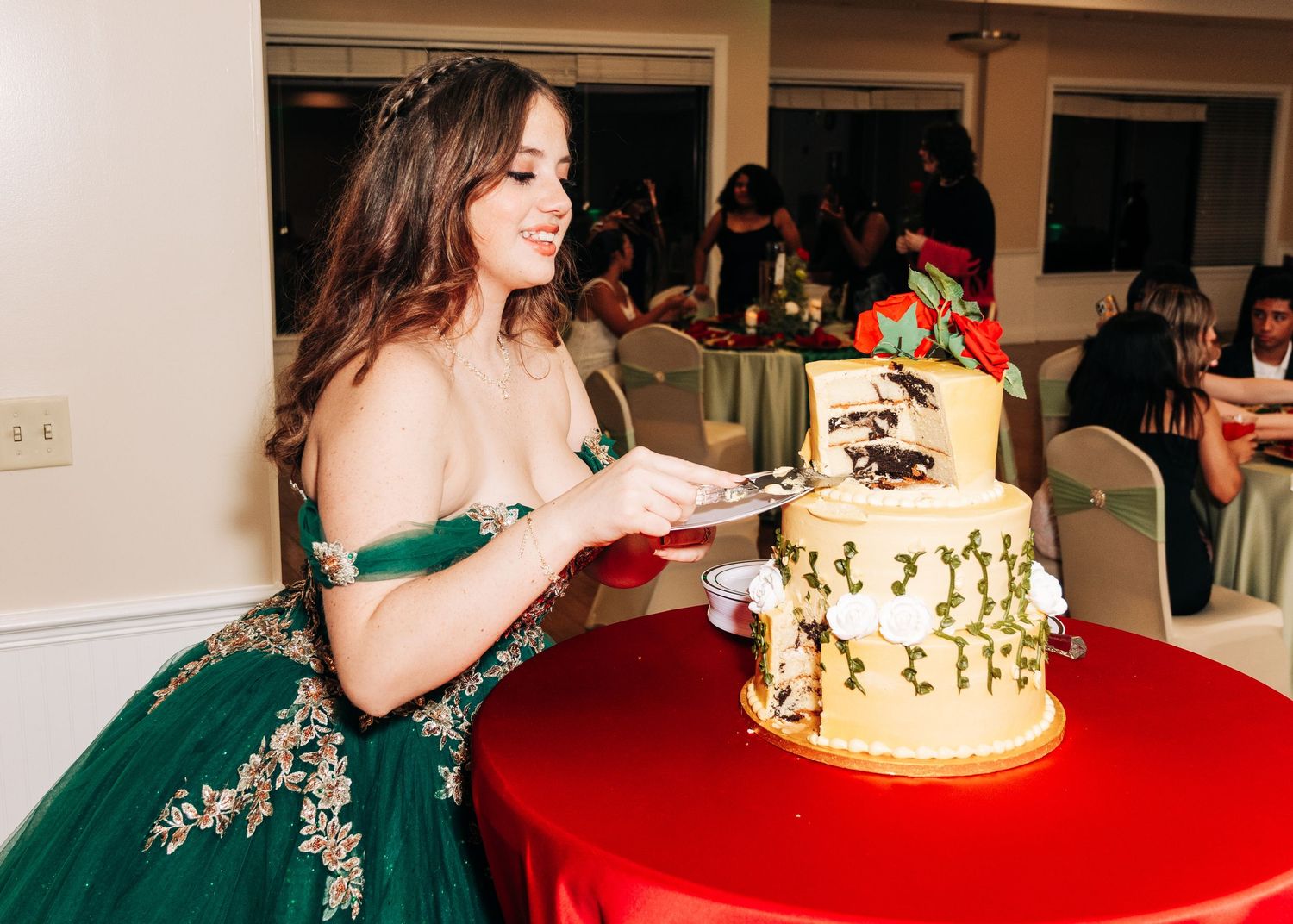 Young woman in green ball gown cutting a decorated two-tier cake at a quinceañera celebration.