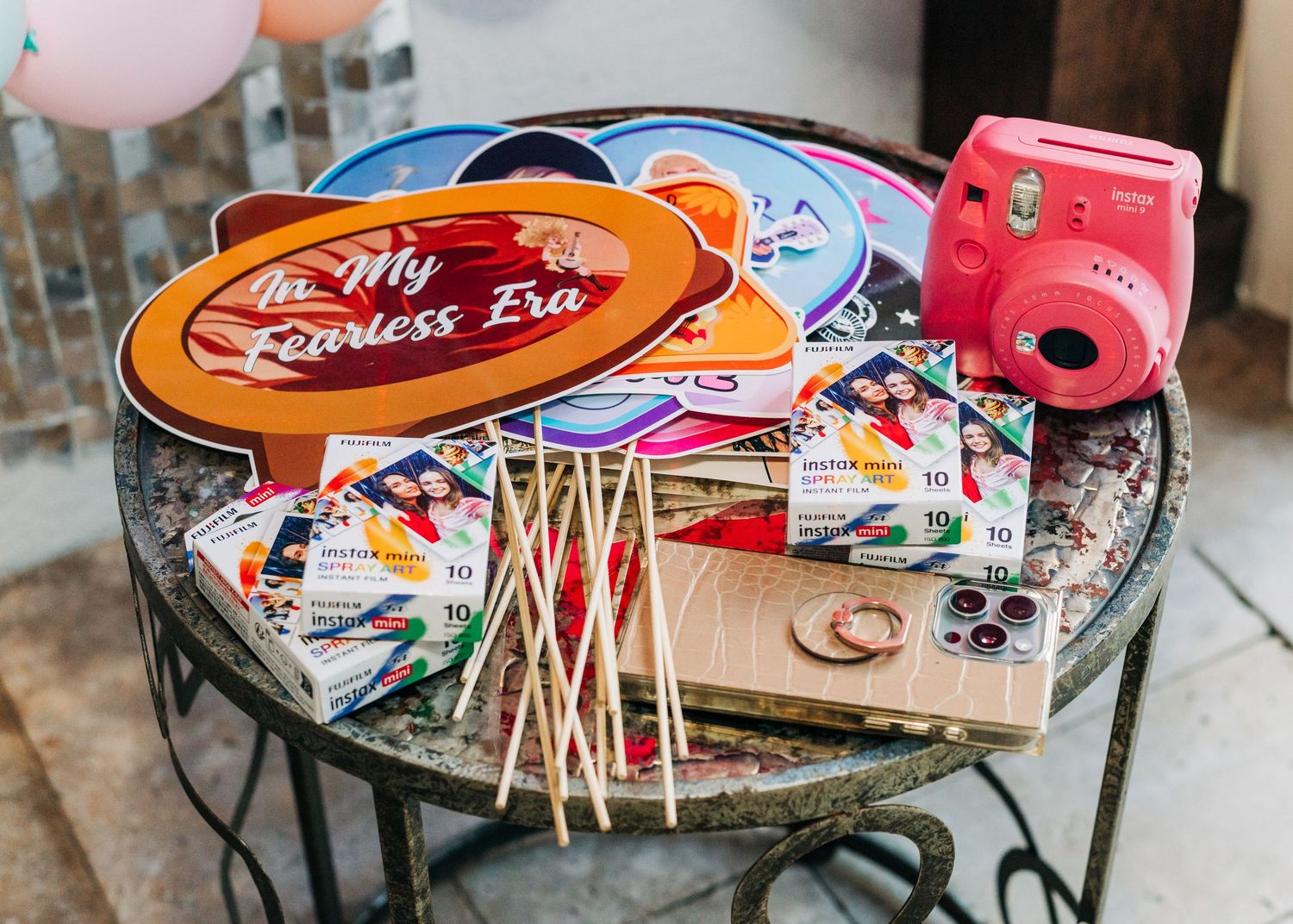 Taylor Swift Fearless Era party setup with Instax Mini camera, film packs, and colorful photo booth props on decorative table.