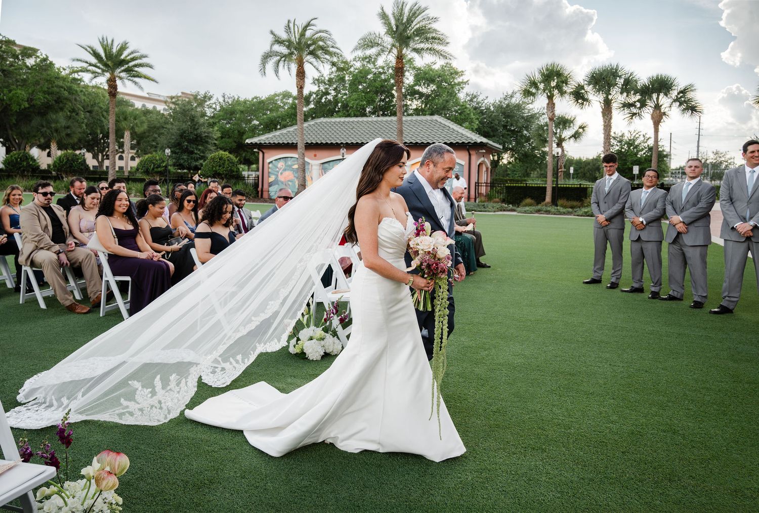 Bride and groom walk down the aisle at an elegant outdoor wedding ceremony surrounded by guests on a lush green lawn.