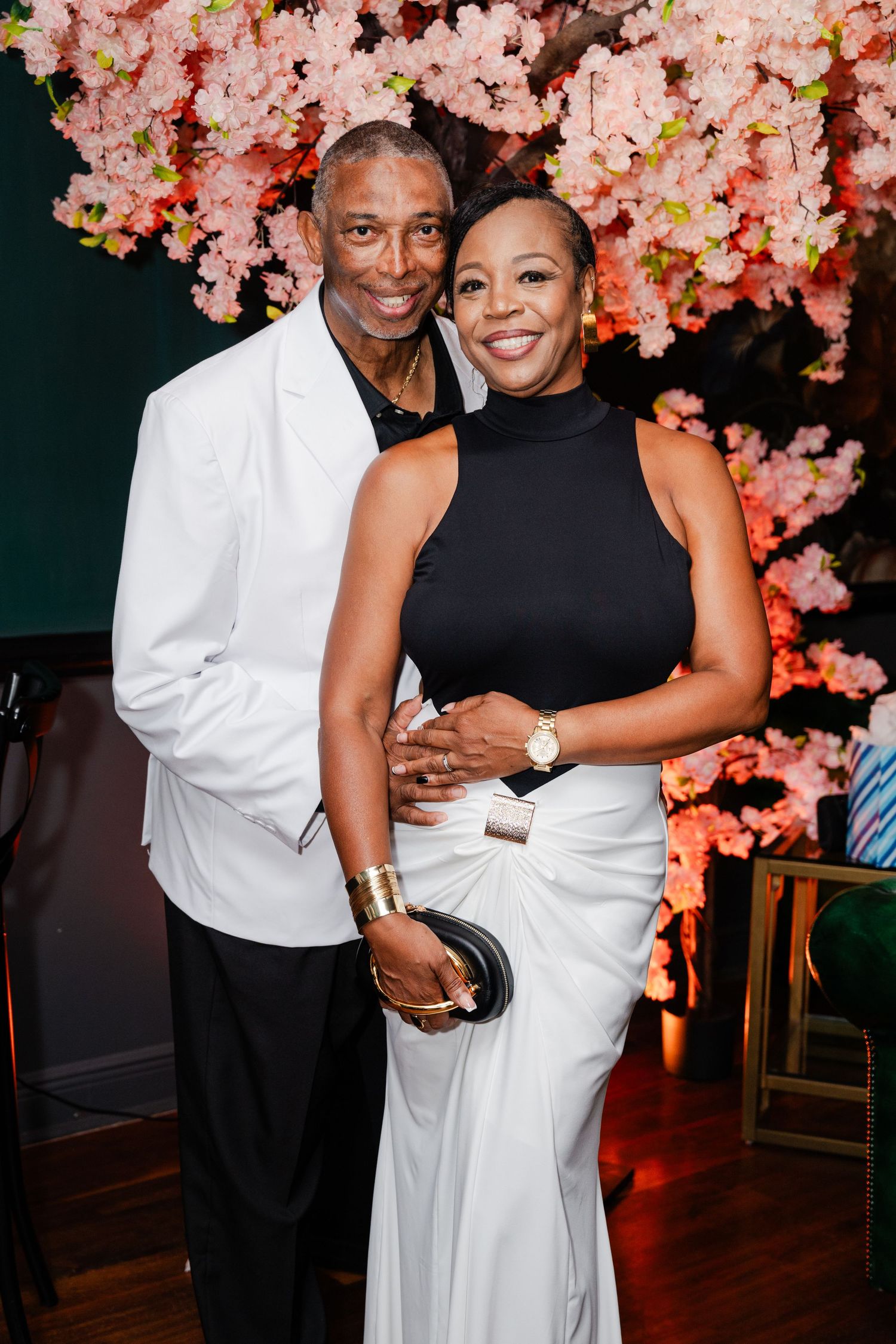 Elegant couple posing together at a formal event with pink cherry blossom decor backdrop.