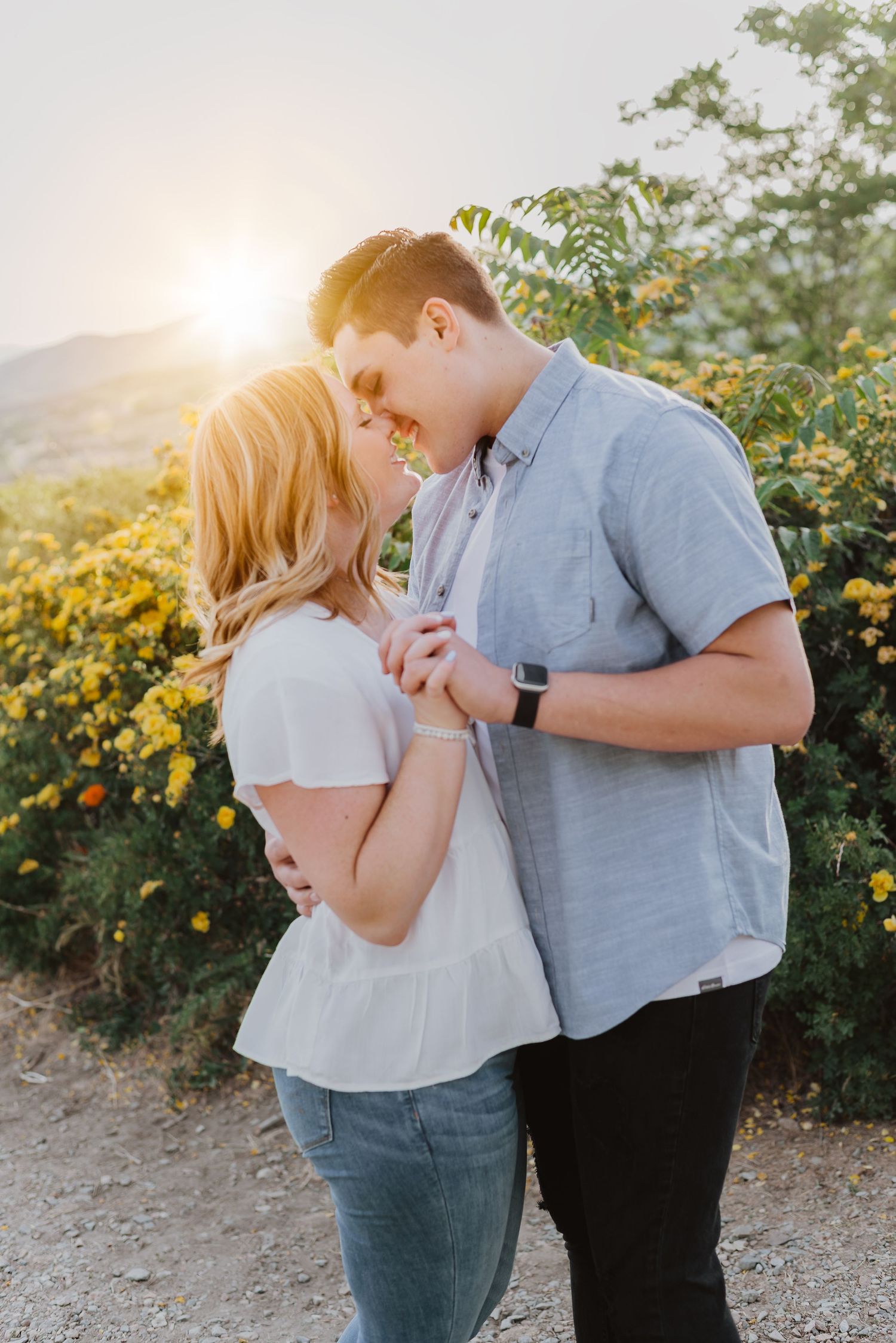 Couple sharing a romantic moment at golden hour with yellow wildflowers and sunlight glowing behind them outdoors.