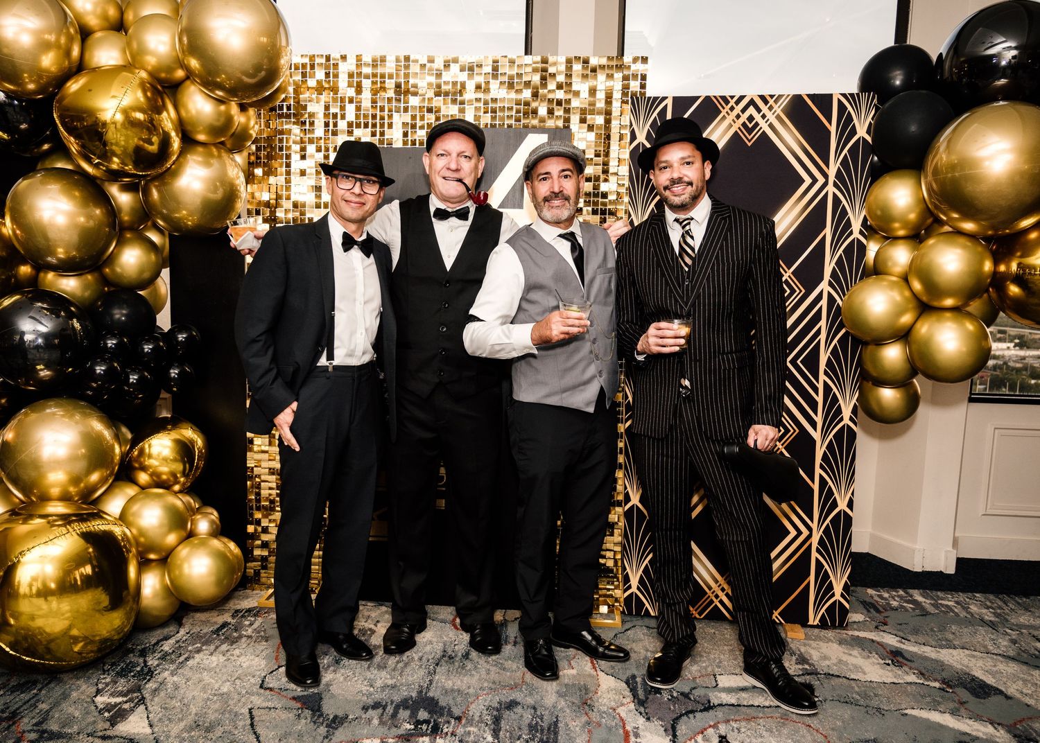 Four men in formal attire pose together at a glamorous black and gold Great Gatsby themed party event.