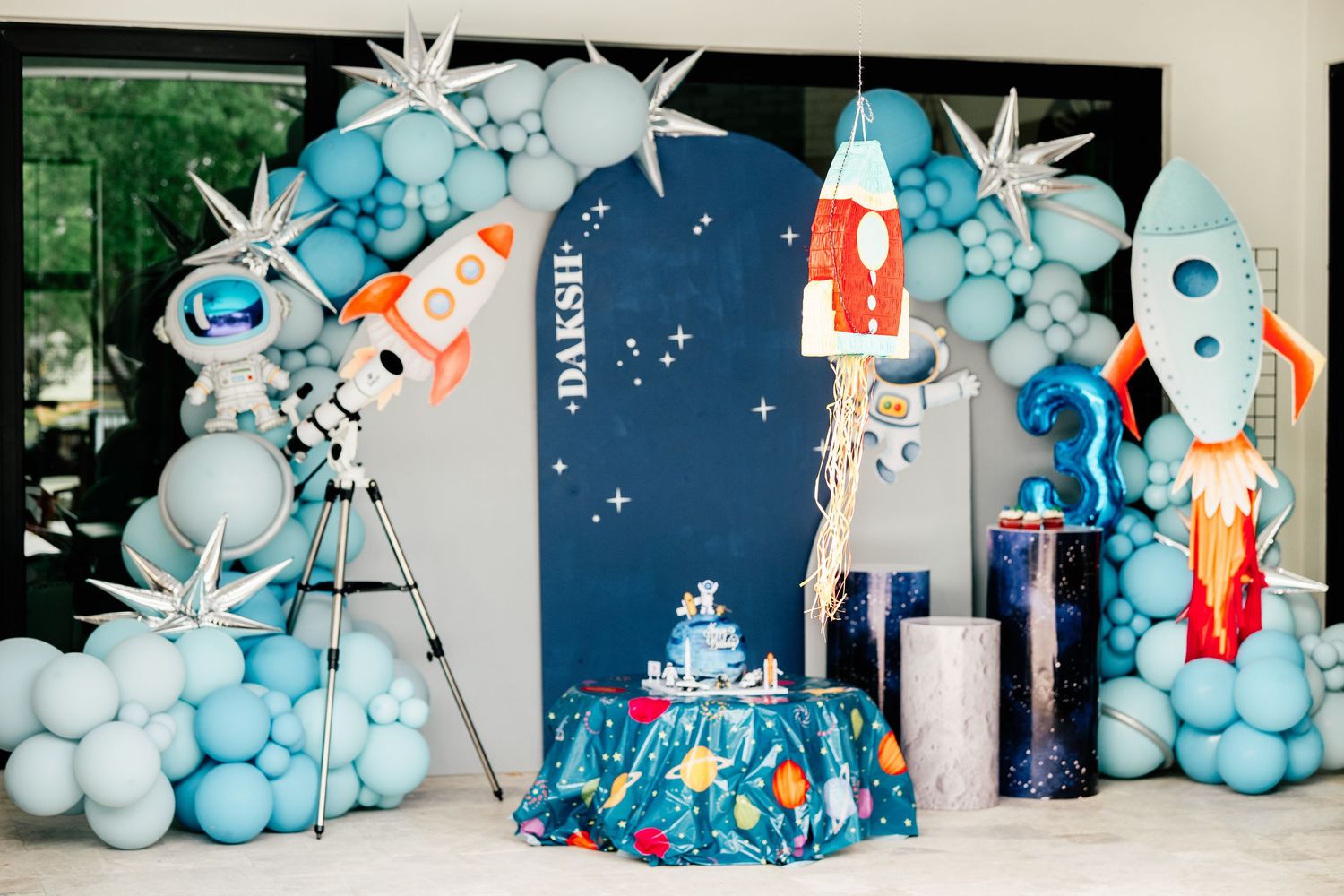 Space-themed birthday party backdrop with balloon arch, rocket decorations, and astronaut for a child named Daksh.