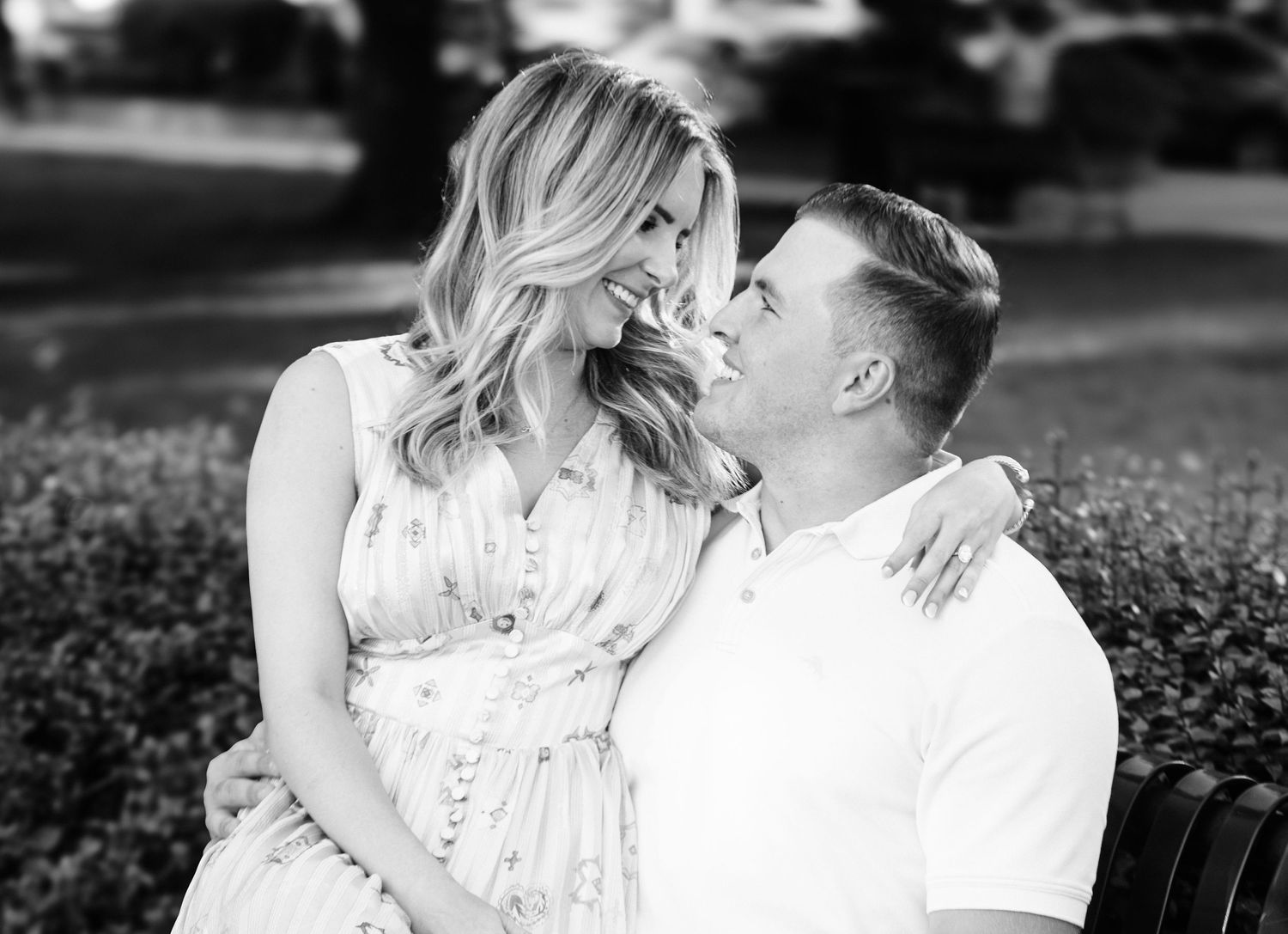 Black and white photo of a smiling couple sitting closely together outdoors, sharing a romantic moment.