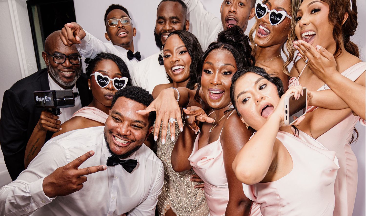 Diverse group of friends celebrating at a wedding, posing for a fun photo booth picture in formal attire.