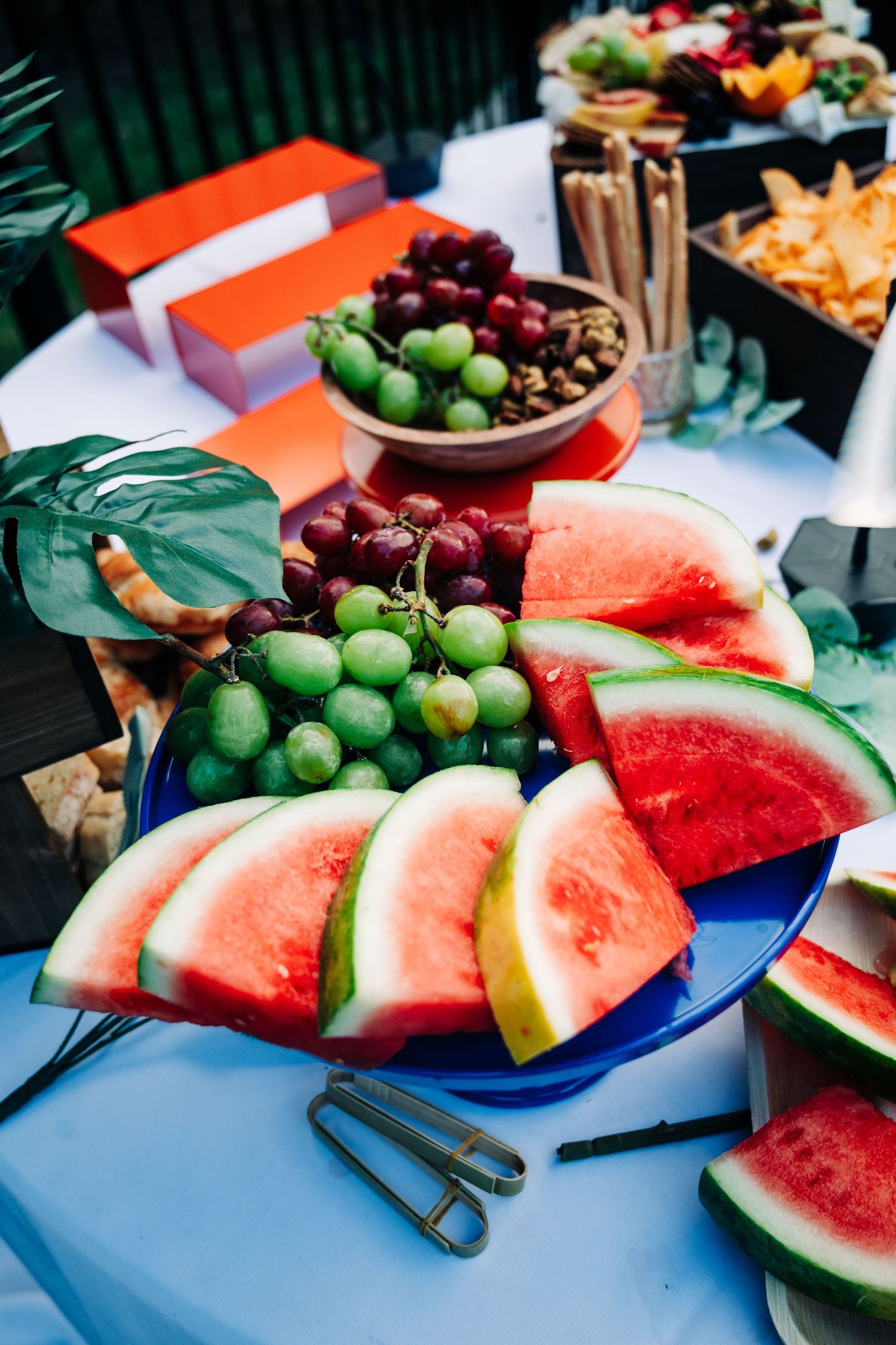 A colorful fruit display with watermelon slices, green and red grapes on a blue plate at a catered event.