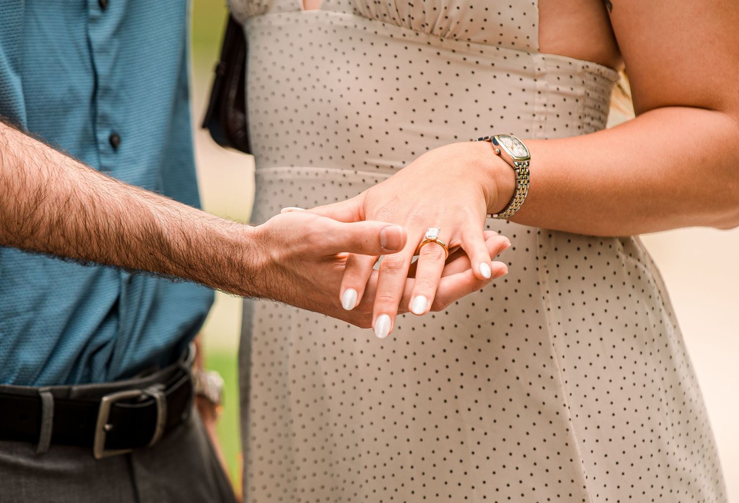 Man placing an engagement ring on a woman's finger during a romantic proposal outdoors.