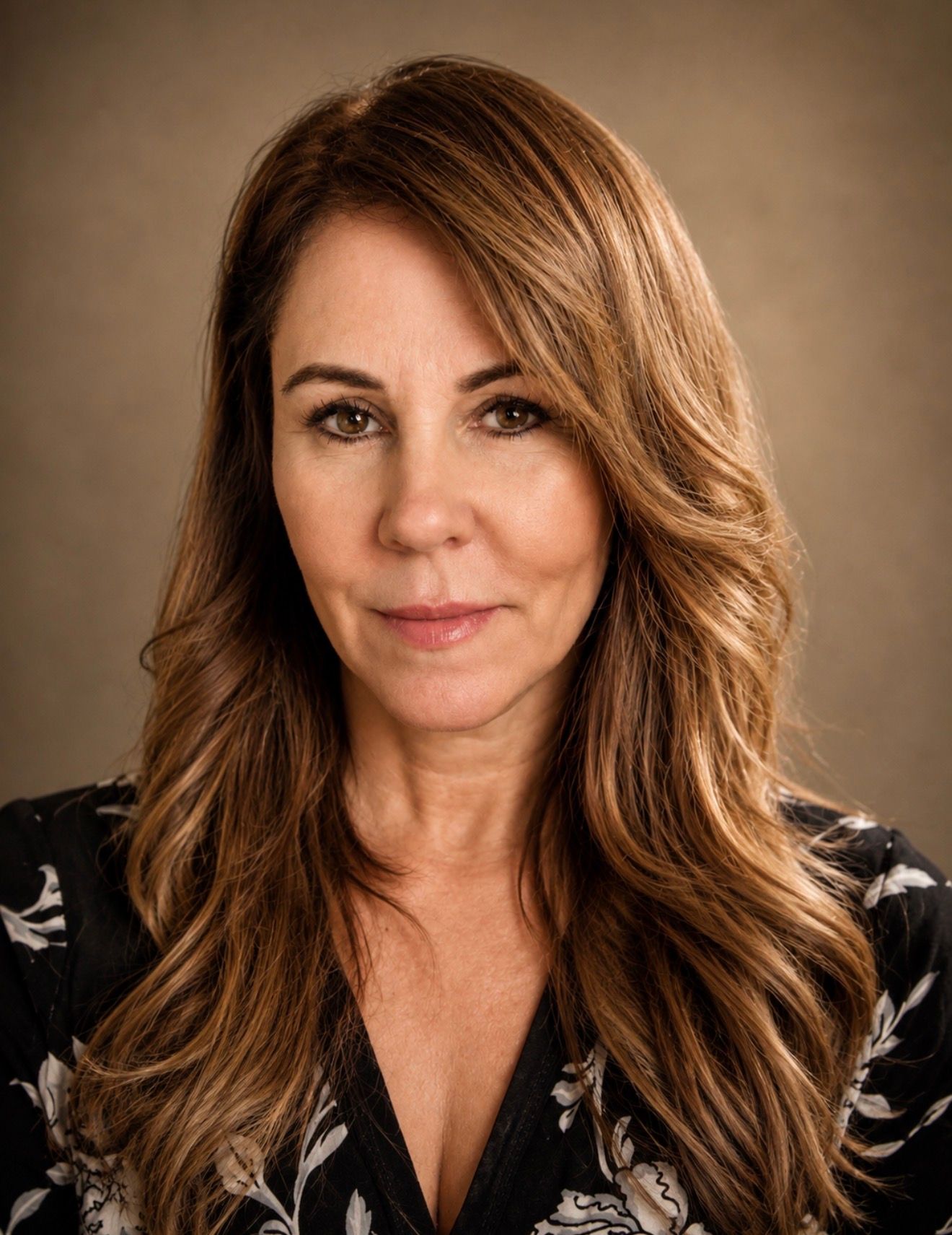 Professional headshot of a woman with long auburn hair wearing a floral blouse against a neutral background.