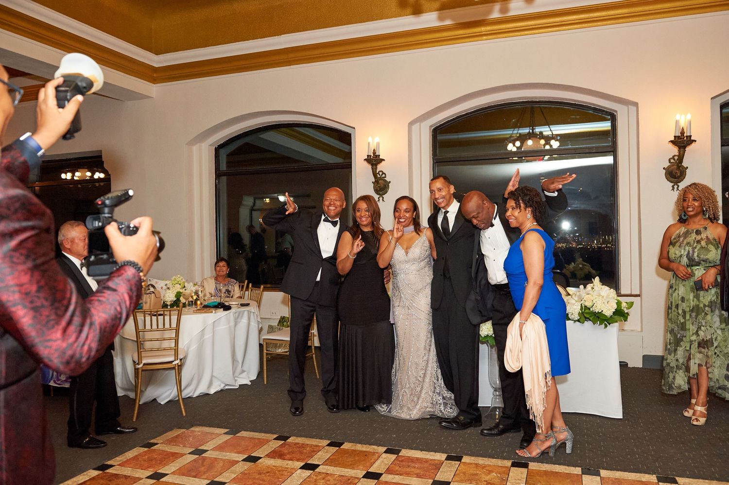 Group of elegantly dressed guests pose together on a decorative dance floor at a reception.
