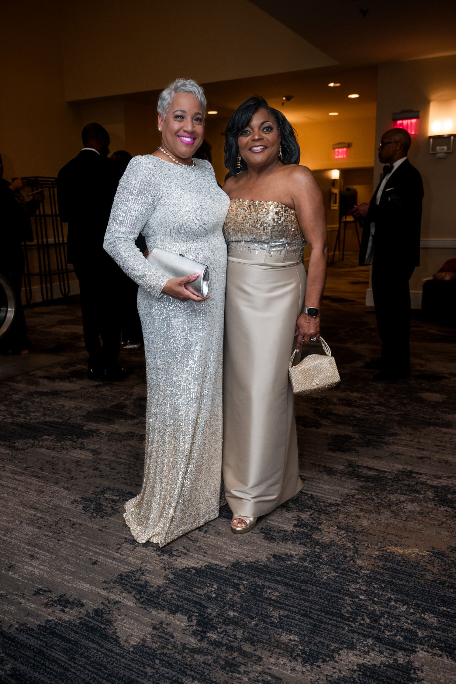 Two elegant Black women in formal sequined gowns posing together at a gala event.