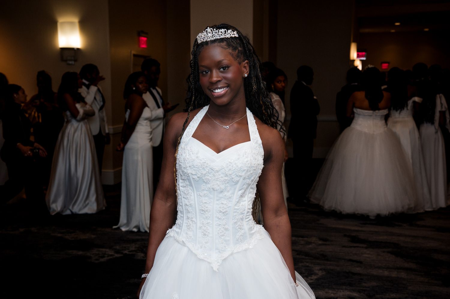 Young Black woman in white ball gown and tiara smiling at a formal debutante ball event.