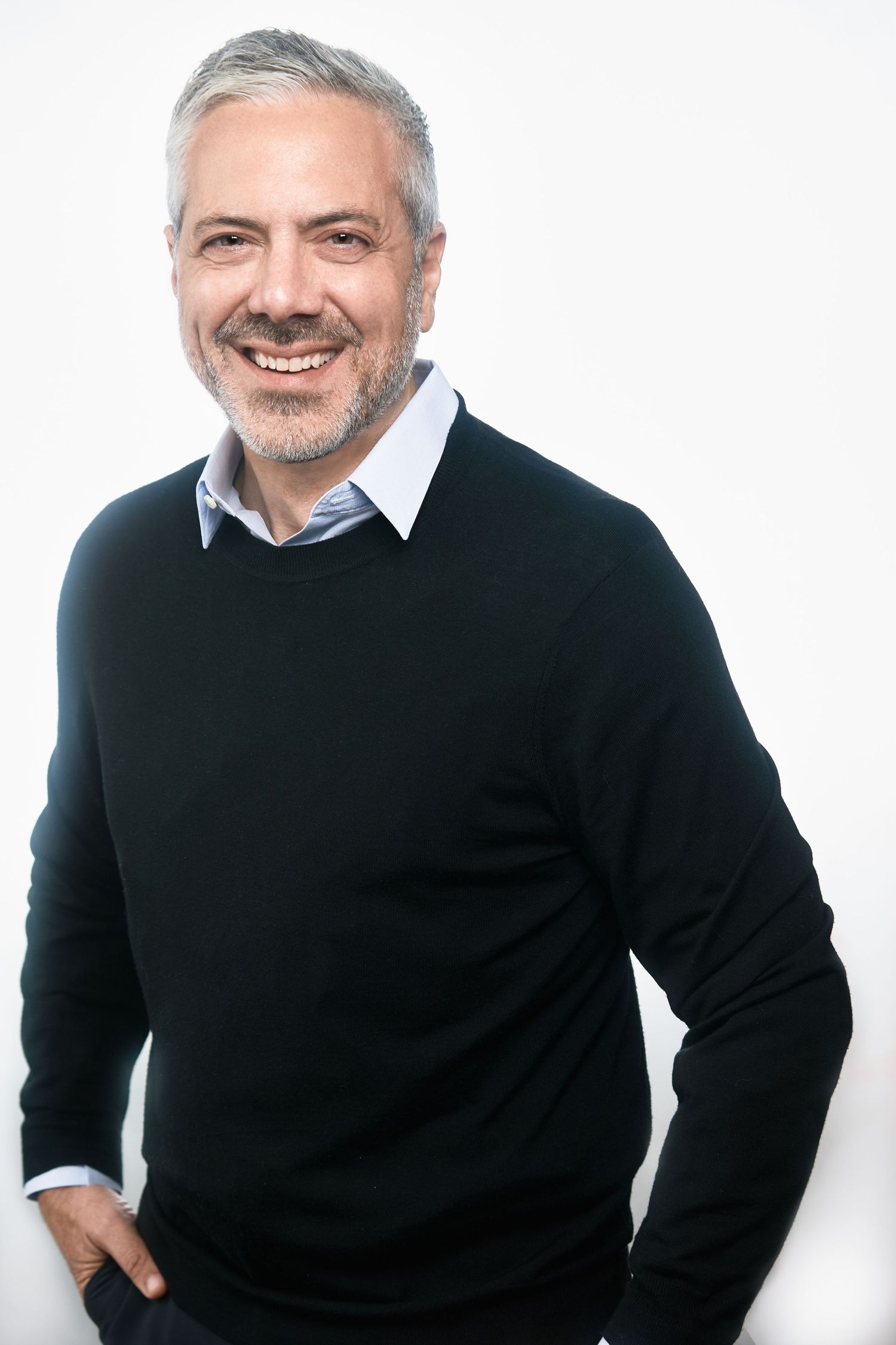 Smiling middle-aged man with gray hair in black sweater against white background.